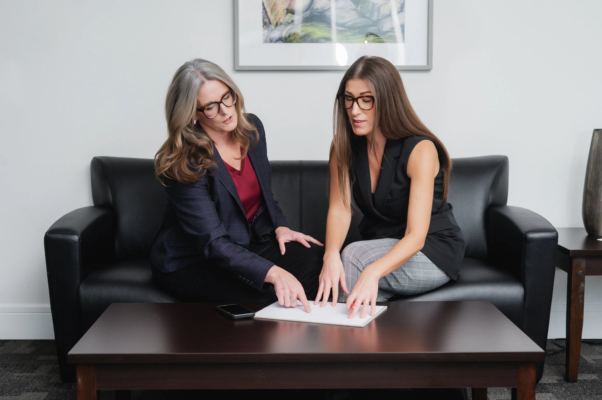 Separation and divorce coach Lana Wickstrom in Saskatoon is looking at a notebook on a table, with a smartphone nearby, while collaborating and pointing at the notebook.
