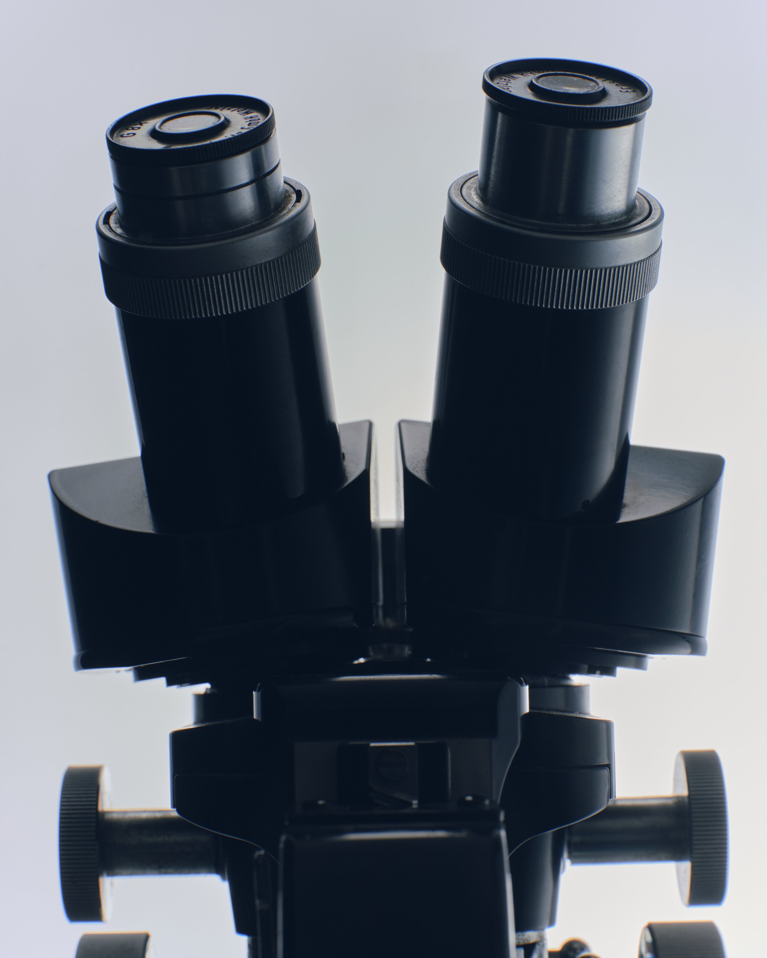 Close-up of a black microscope viewed from below against a gray background.