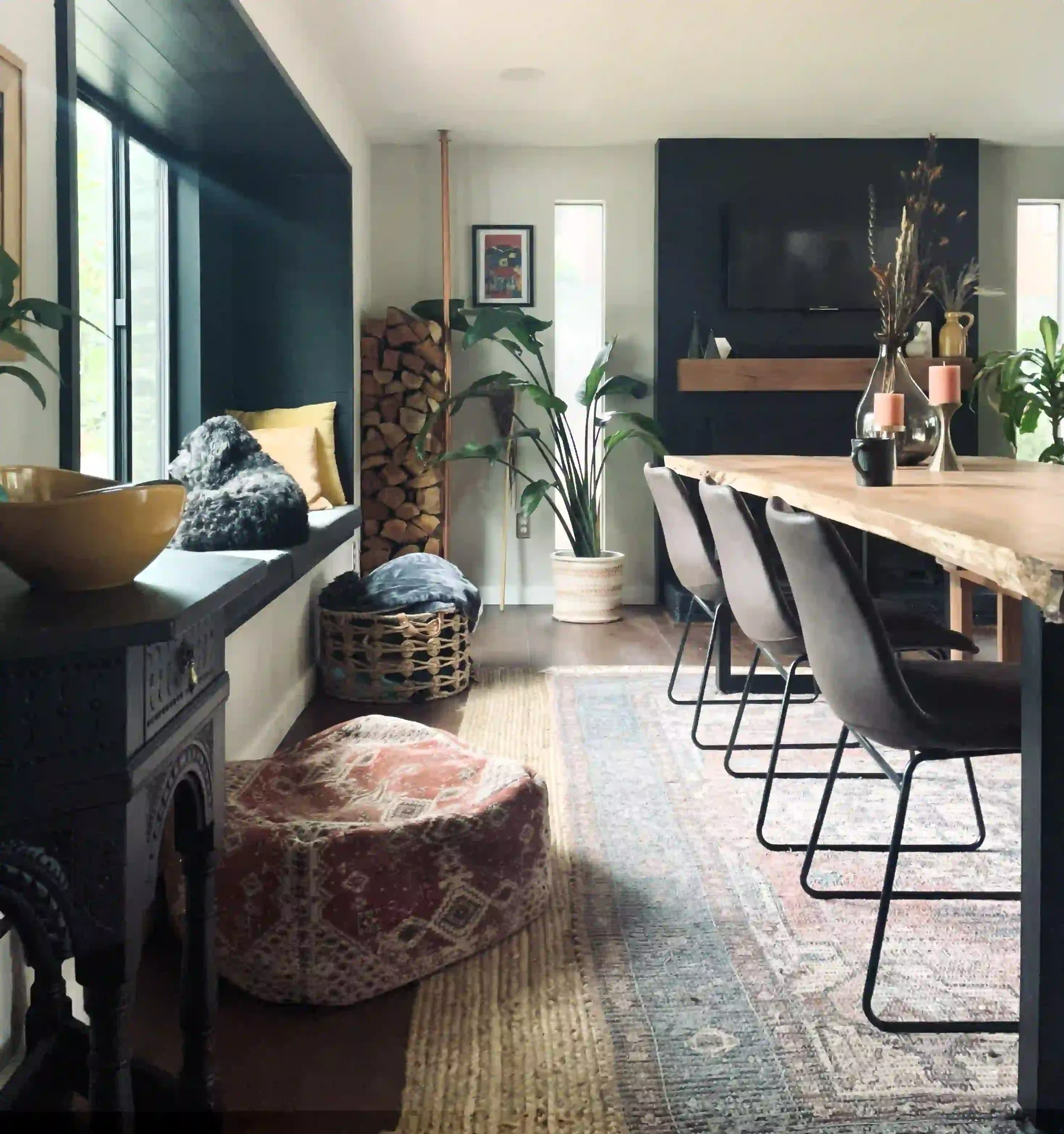 A cozy living room and dining area with a large wooden table, black chairs, plants, and decor, including candles and vases.