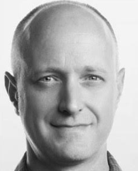 Black and white portrait of a smiling man with short blonde hair and light eyes