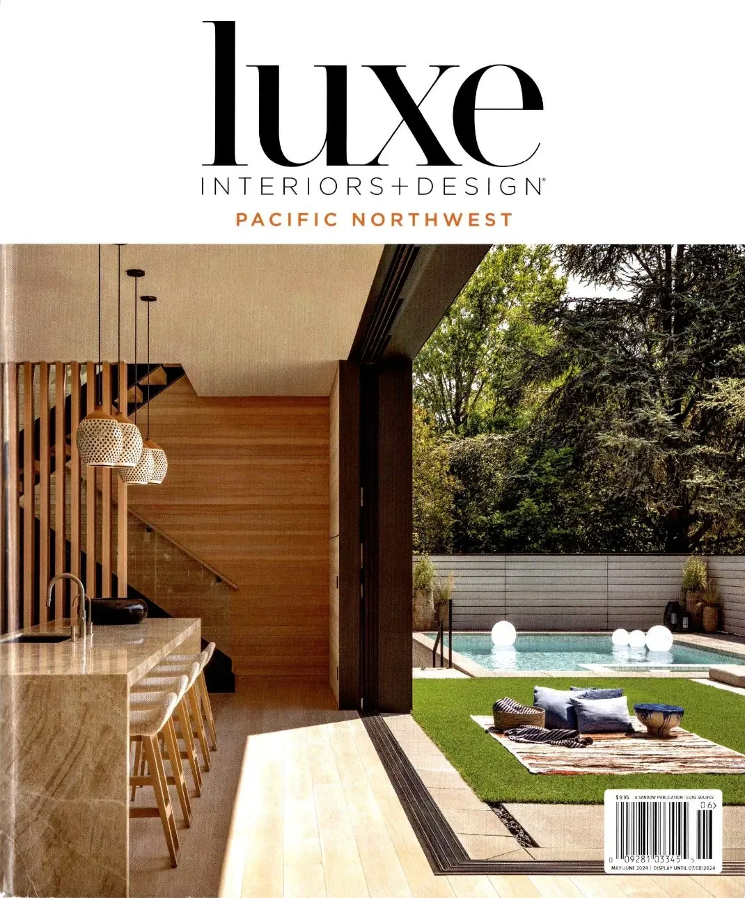 Interior view of a modern home with a kitchen island, pendant lights, connecting to an outdoor pool area with grass, seating, and large decorative lanterns.