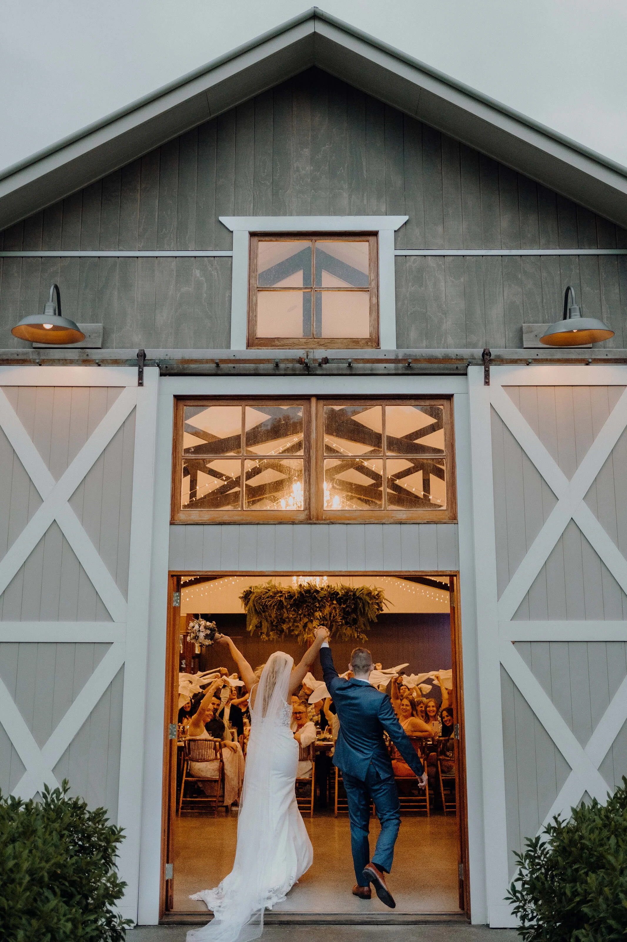 Cowbell Creek Wedding Venue - A newlywed couple is entering a rustic barn decorated for a wedding reception, with guests celebrating inside.