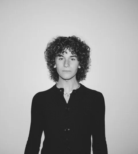 Black and white photo of a woman with curly hair wearing a black top against a plain background.