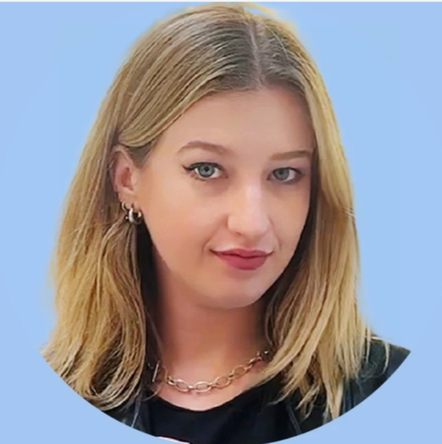 Close-up of a young woman with blonde hair, blue eyes, earrings, gold chain necklace, and black top, against a light blue background.