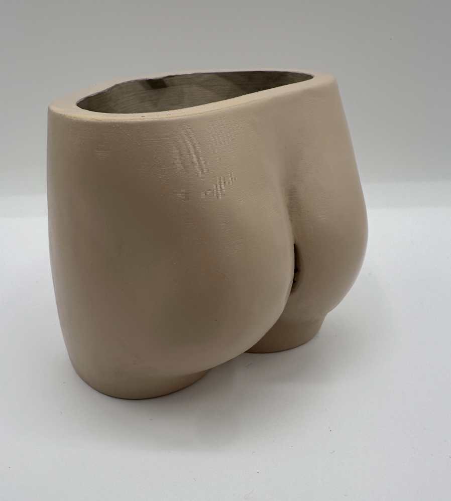 Cream-colored ceramic planter in the shape of a human buttocks, with an opening at the top for plants.