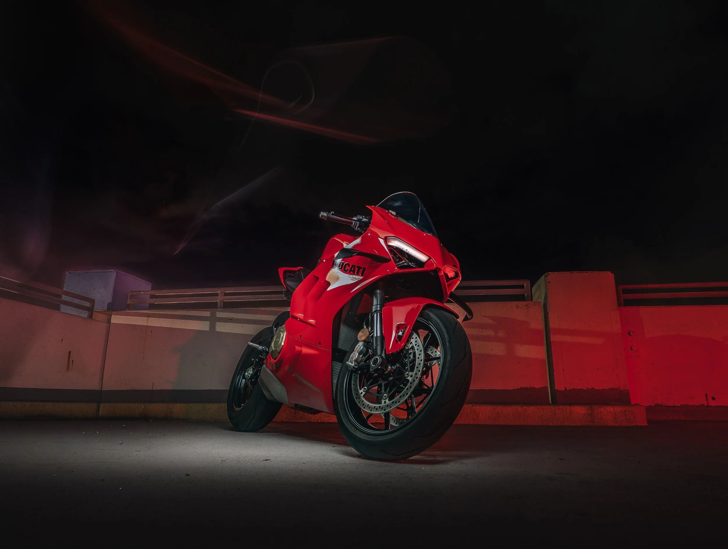 Red Ducati motorcycle parked on a rooftop at night with a dark sky and red lighting reflections on the wall.