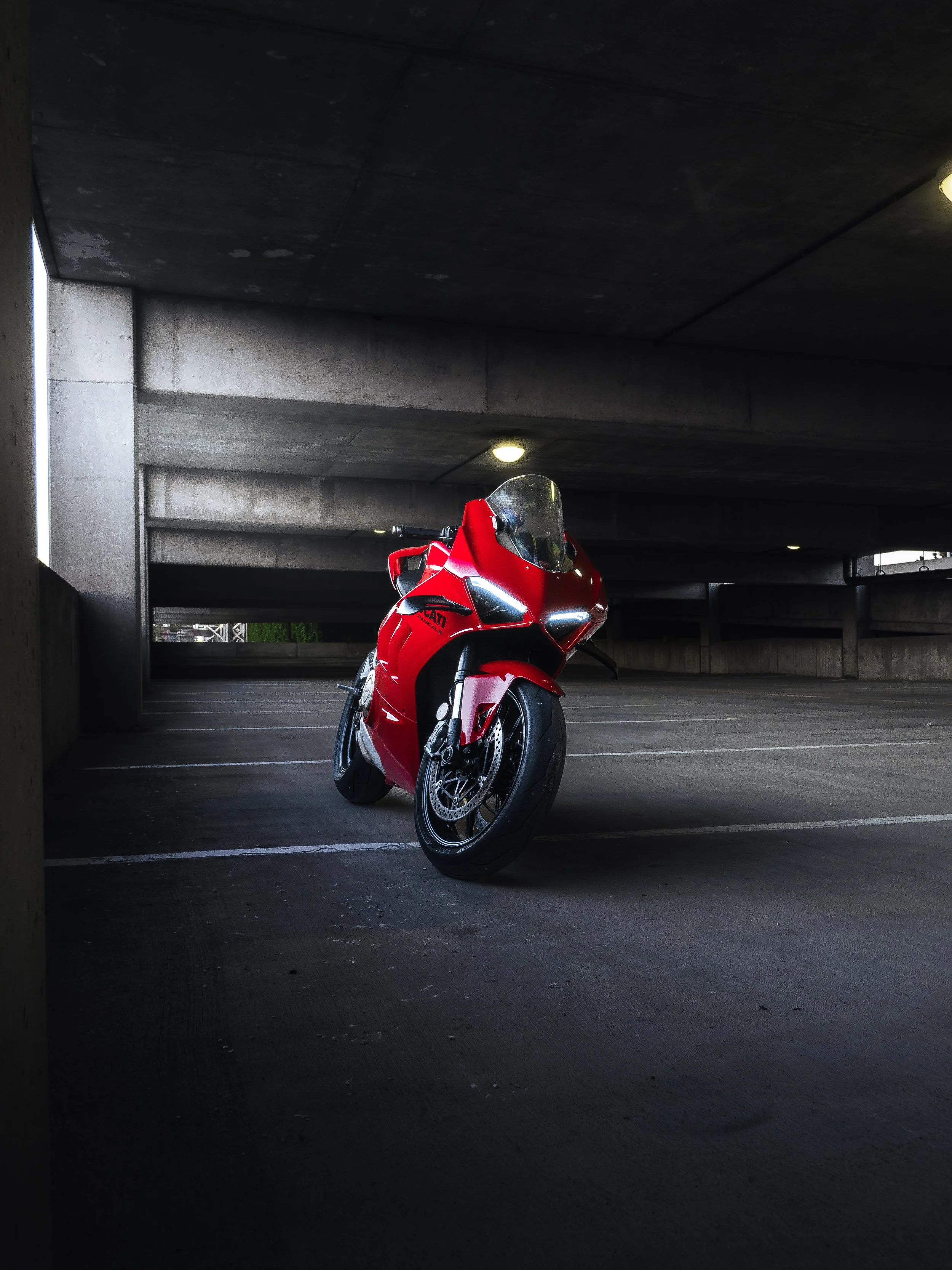 A red Ducati motorcycle parked in an underground parking garage with concrete walls and ceiling.
