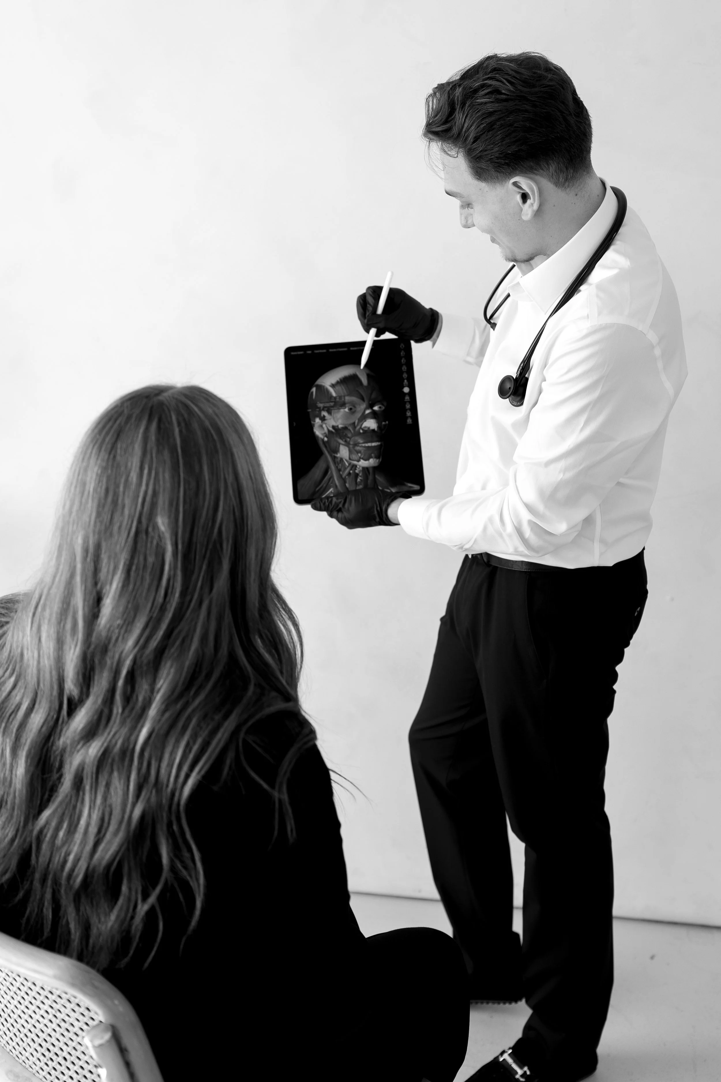 Medical professional showing an X-ray or scan of a face to a seated woman in an office or clinic.
