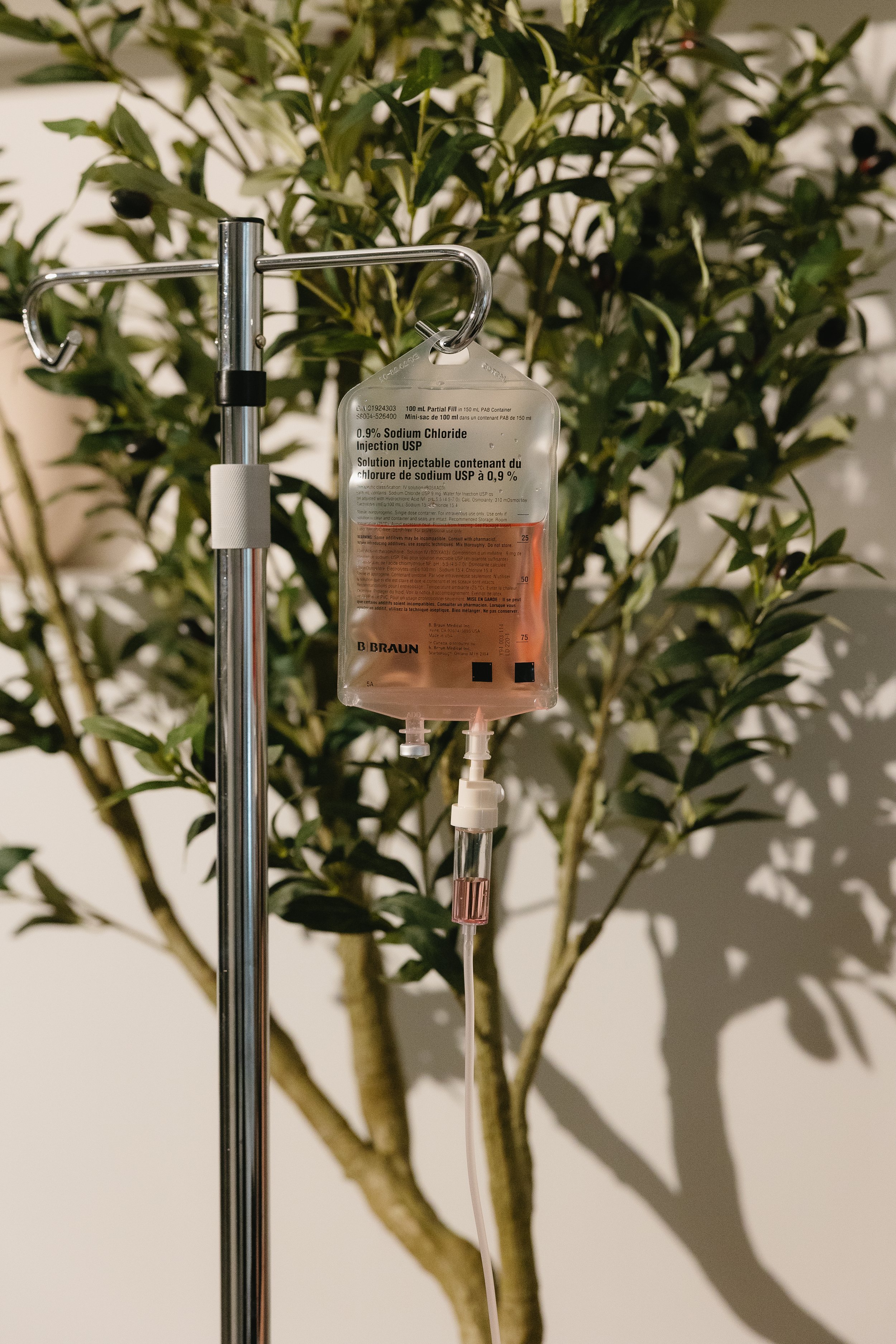 A healthcare professional wearing black gloves and white coat handling an intravenous medication bag with yellow label hanging on a metal IV pole.