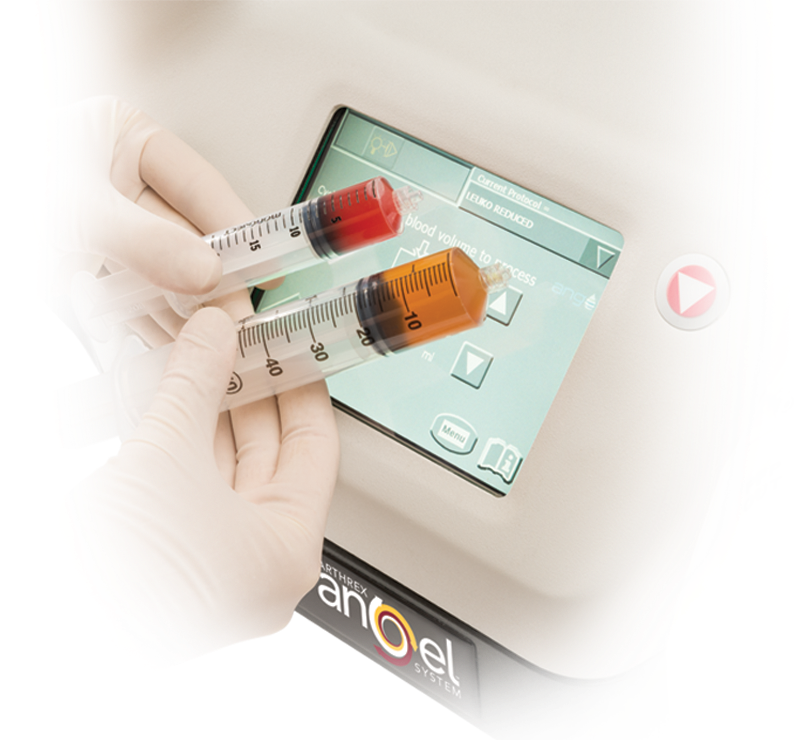 A healthcare worker wearing gloves holding two blood sample tubes with red and orange liquids, using a centrifuge machine with a digital display and control buttons.