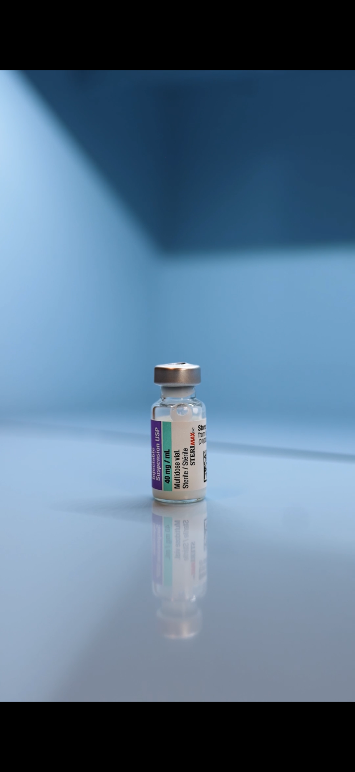 A healthcare professional wearing black gloves and a white coat prepares a syringe with a dose of medication from a small medicine vial.