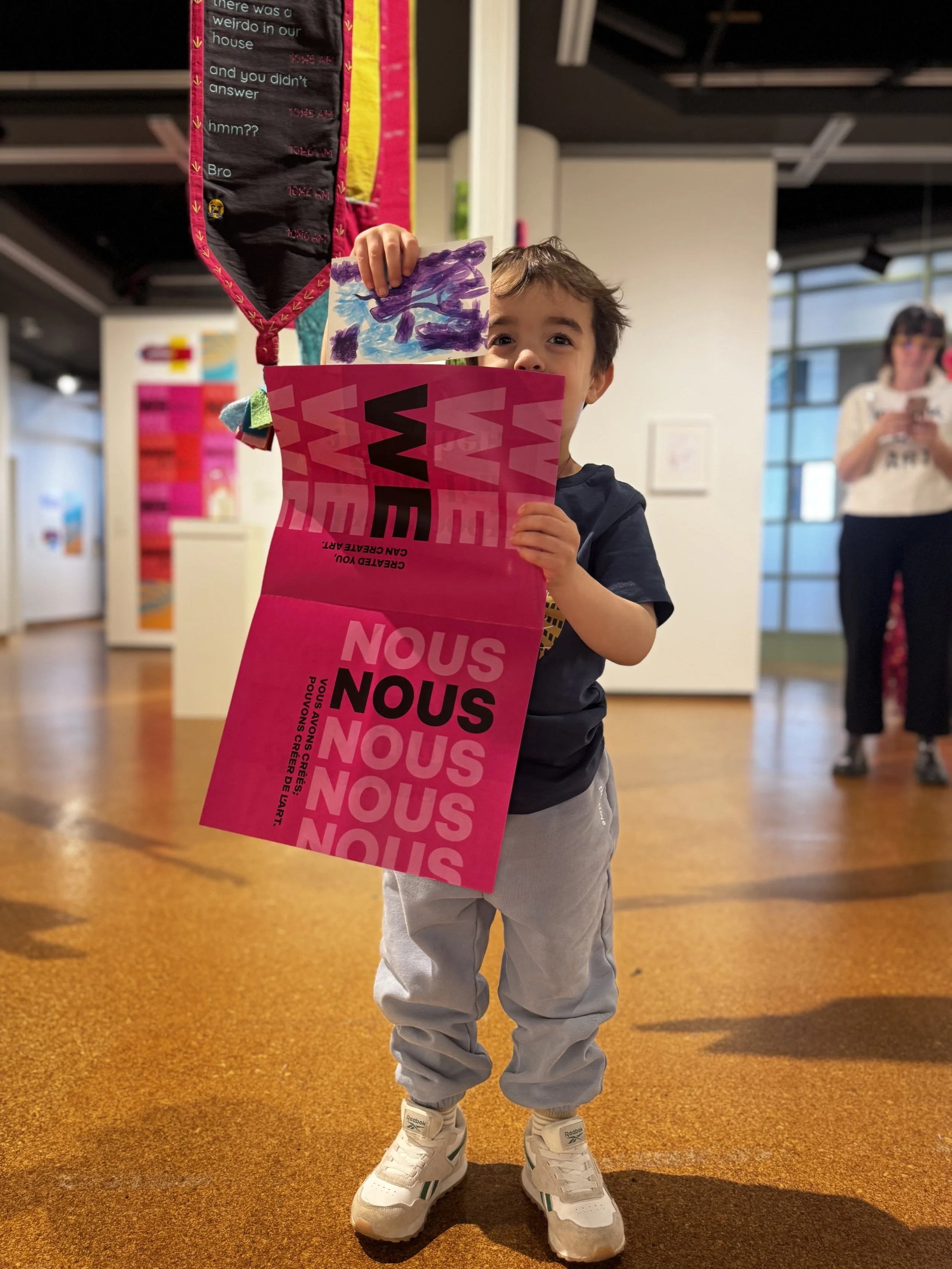 A small child holds a hot pink brochure with mother artist campaign slogans