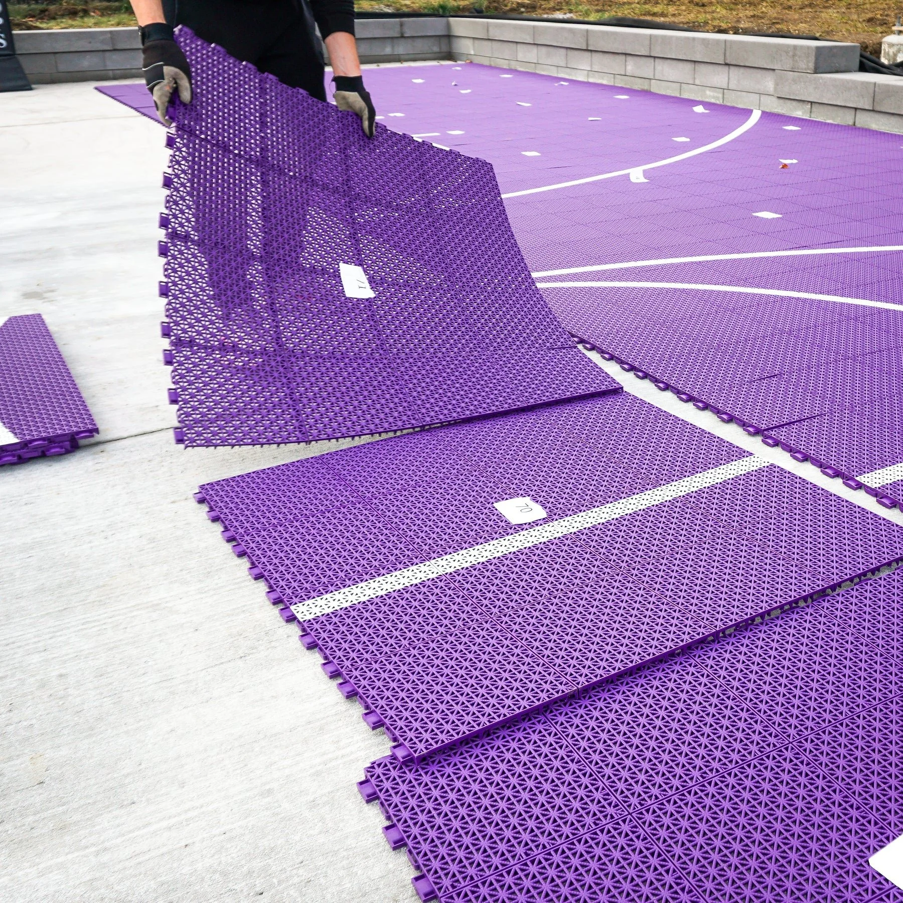 Person laying down purple outdoor pickleball flooring on concrete ground