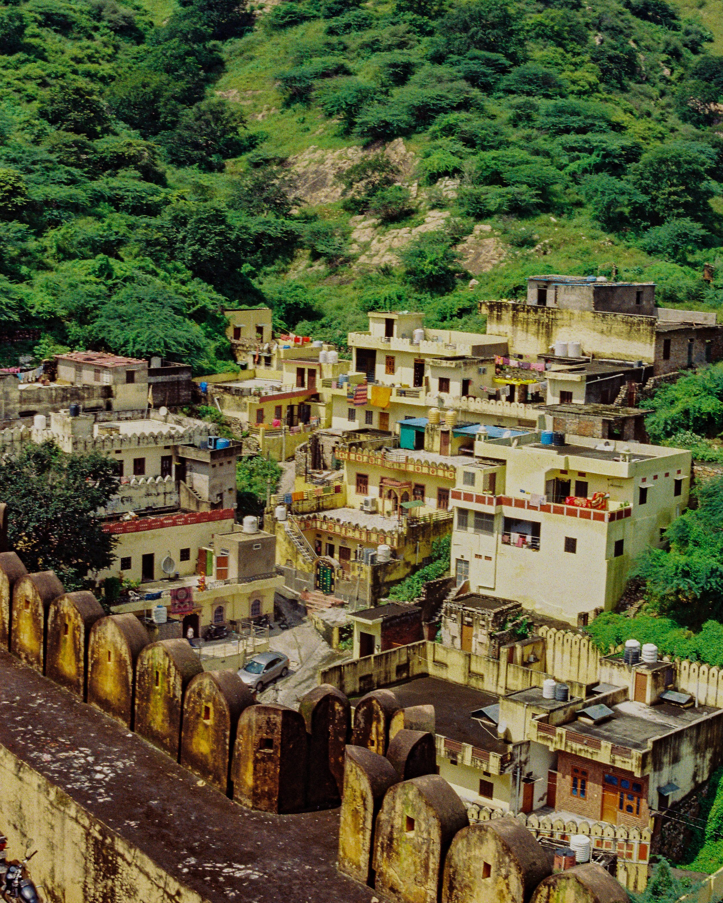 View from a fortified wall looking over a residential area at the base of a green, hilly mountain. The wall has rounded battlements and shows signs of weathering. 35mm film photography. Kodak Ultramax 400. Fujifilm Frontier SP-3000 high-resolution sc