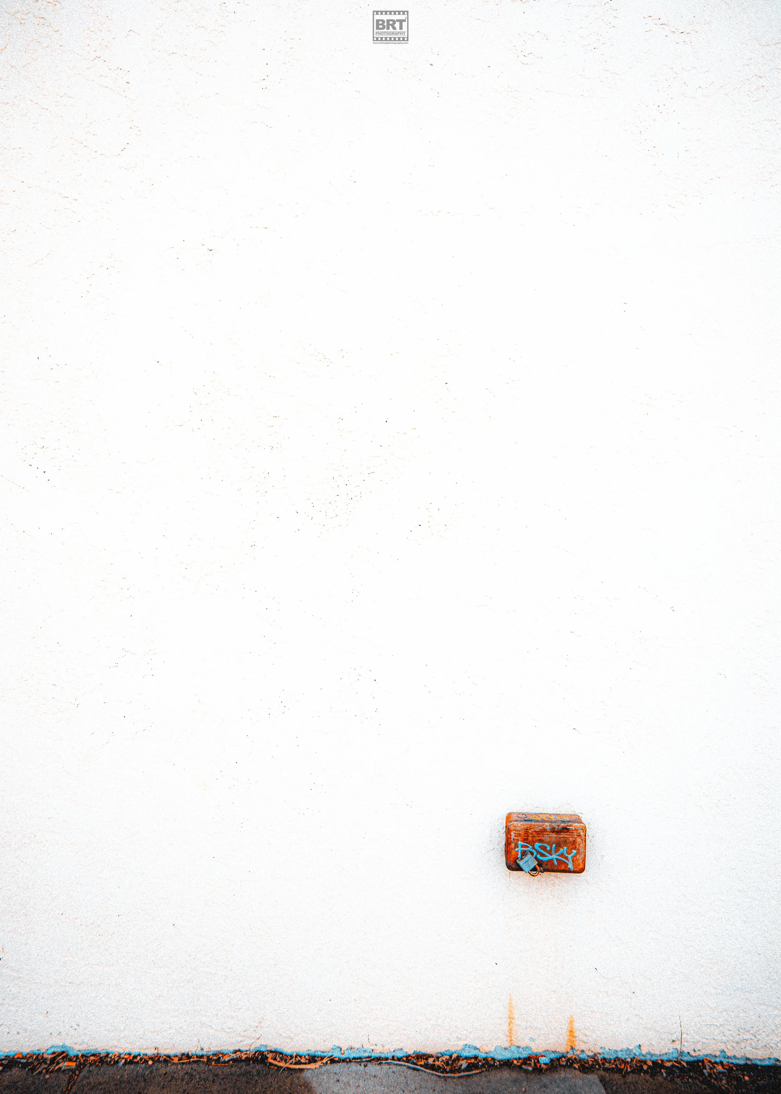 A white wall with a small graffiti-covered orange box and some graffiti on the bottom edge.