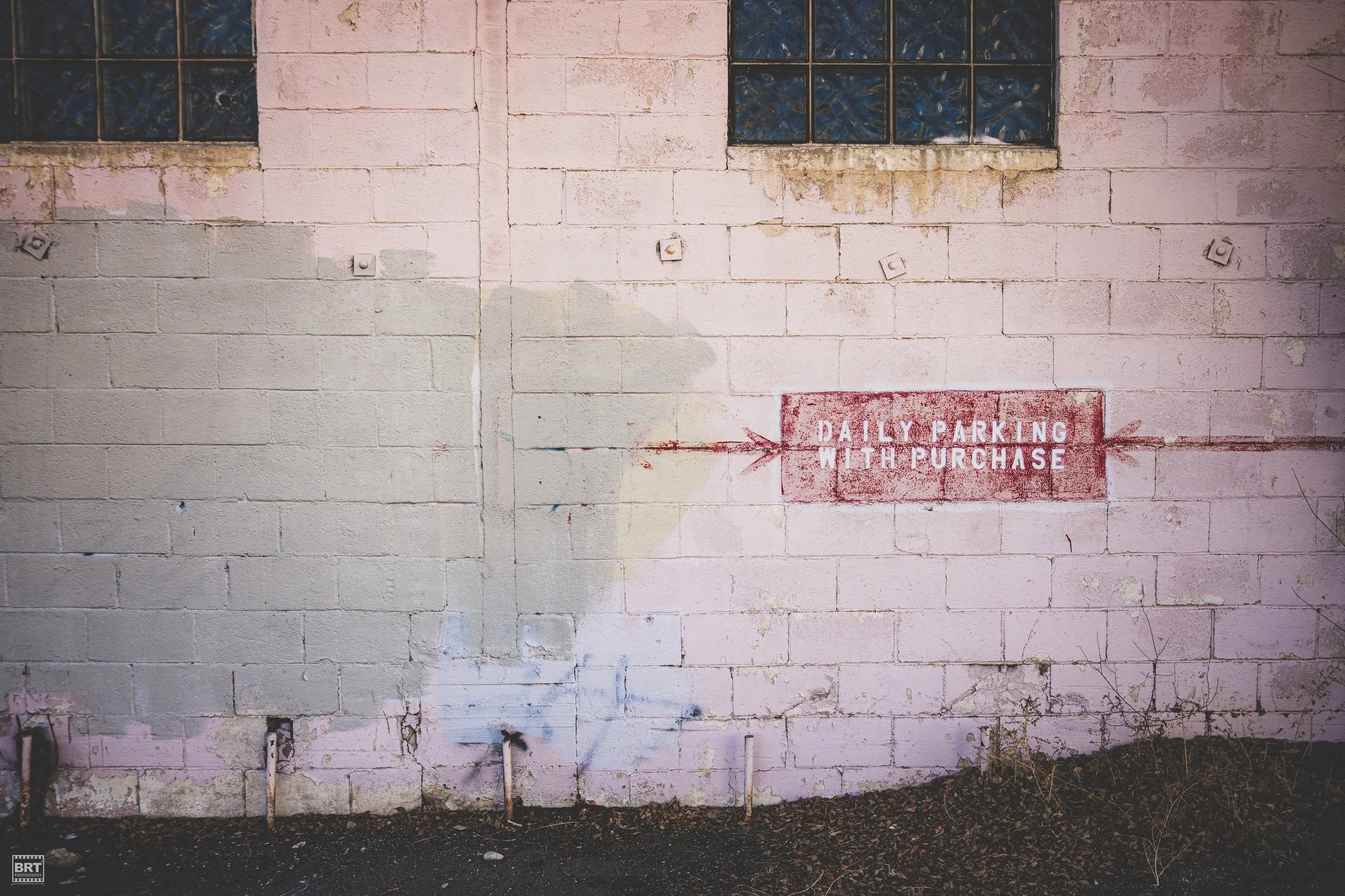 Pink brick wall with blue glass windows and a painted sign that reads 'Daily Parking With Purchase' with an arrow pointing to the left.