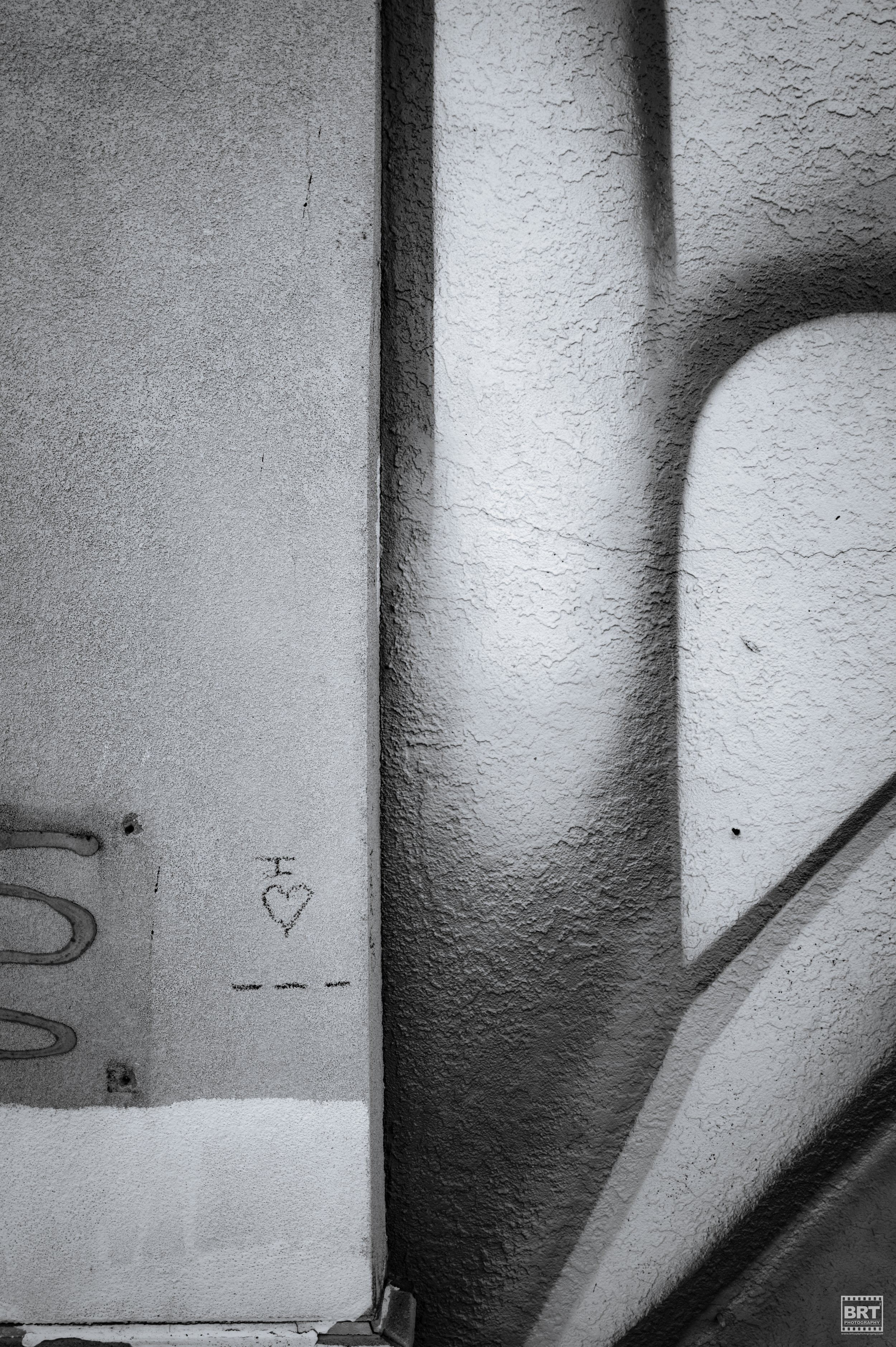 Close-up of a textured wall with a small graffiti symbol of a heart and arrows.