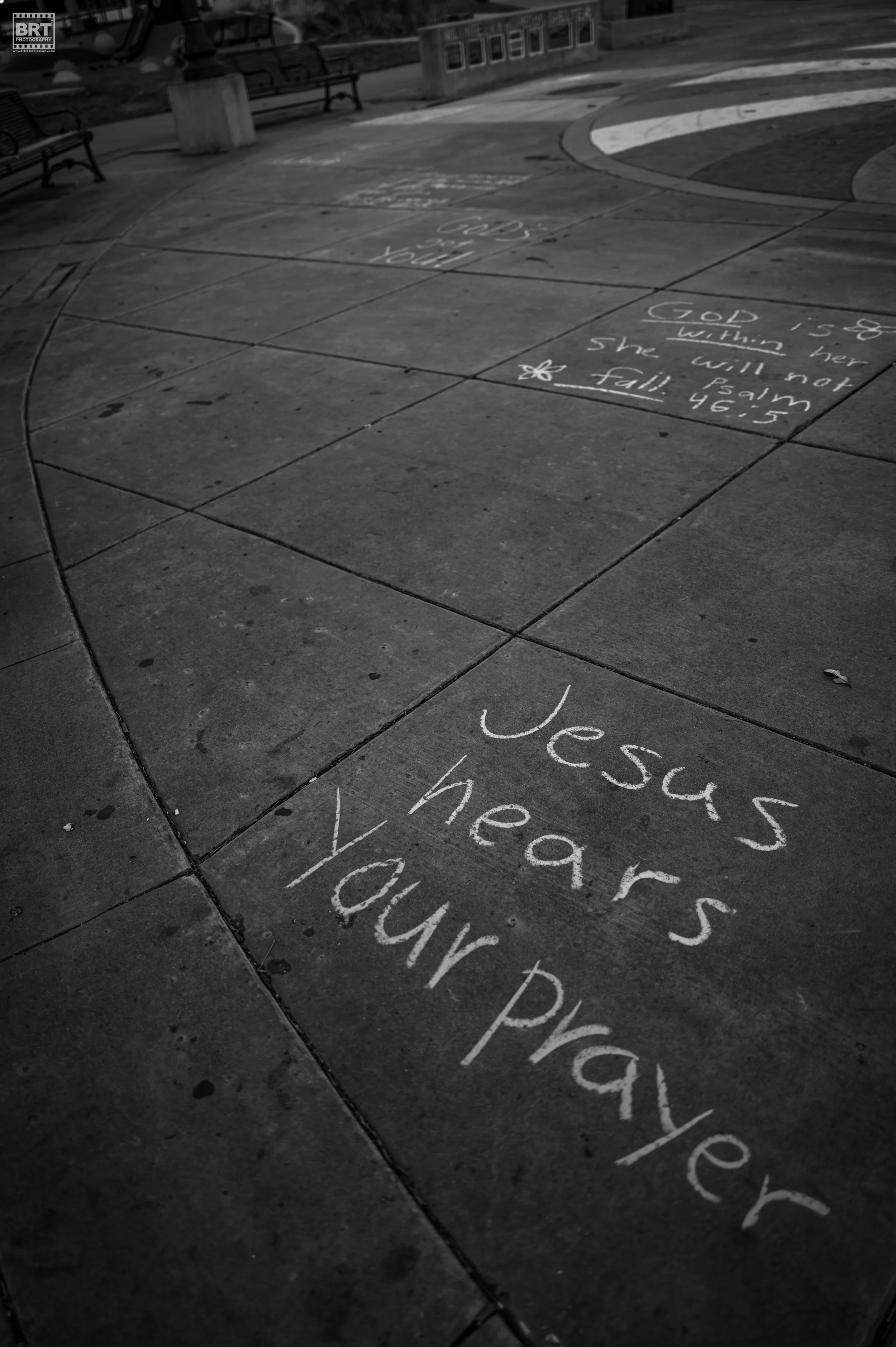 Sidewalk with chalk writings that include a Bible verse about Jesus and prayers and a message that says 'Jesus hears your prayer'.