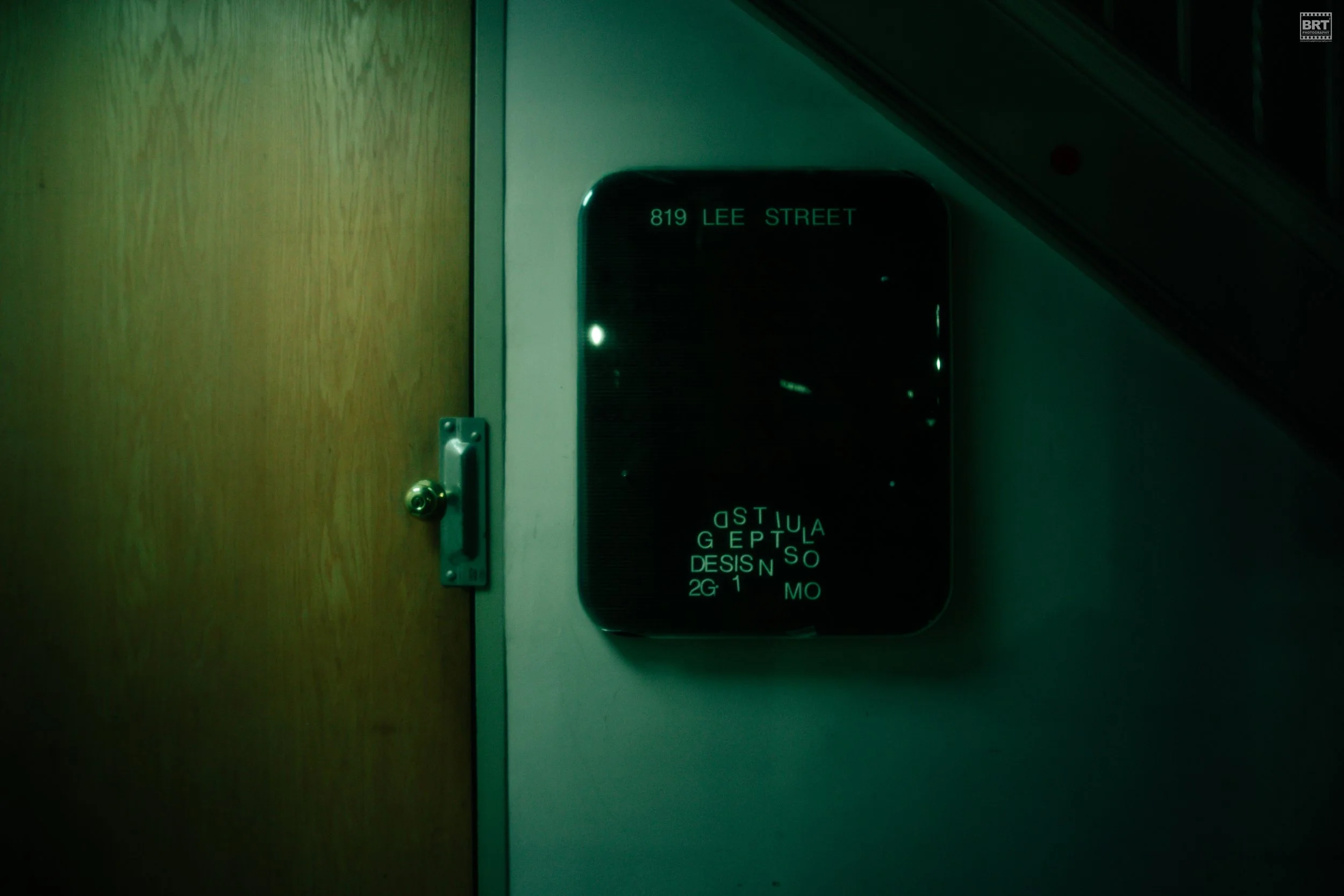 Digital display sign showing the address '819 Lee Street' in green text on a black background, mounted on a wall next to a wooden door.