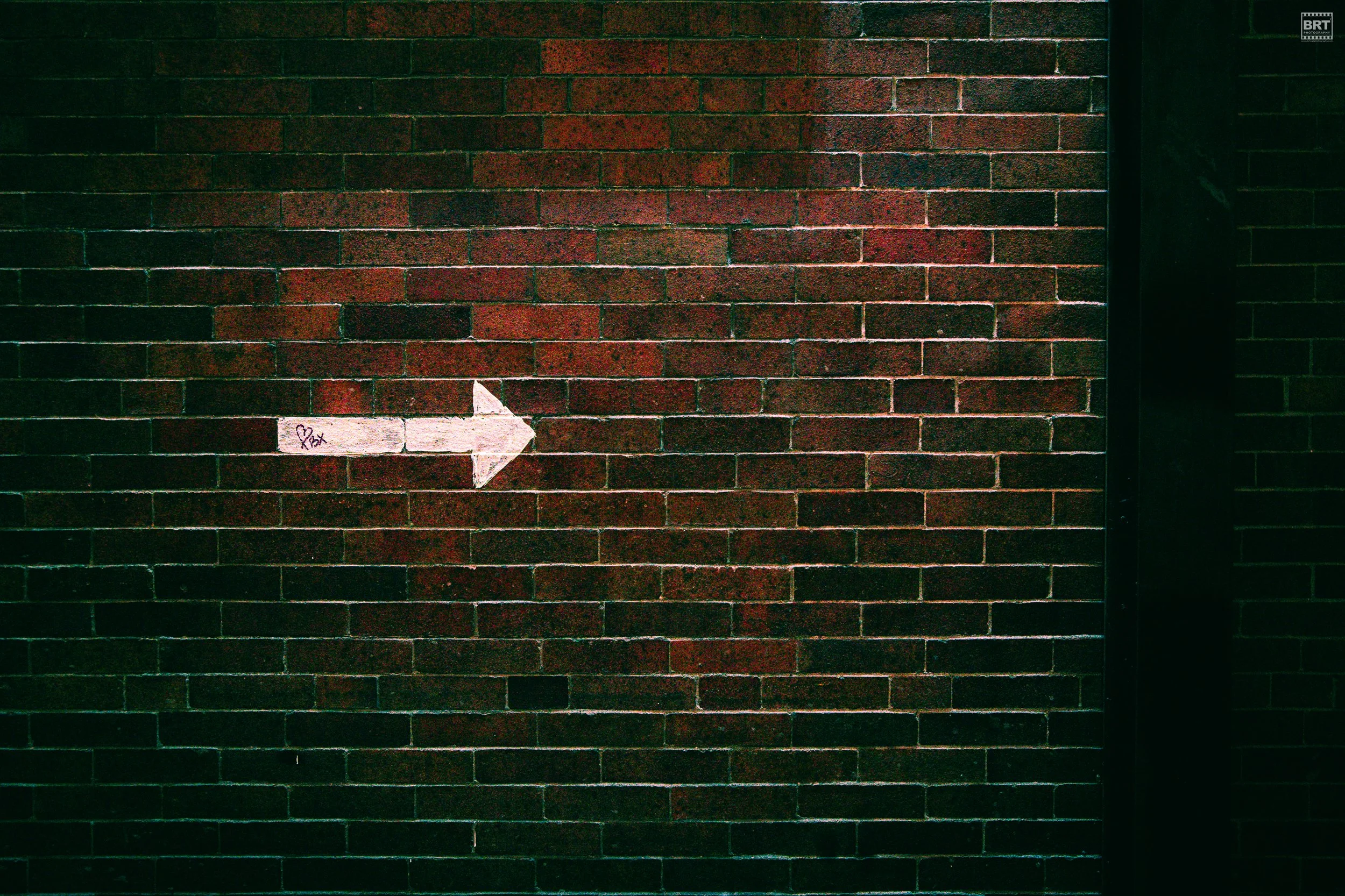 A brick wall with a pink arrow painted on it, pointing to the right, with additional markings that read '❤️ Bx'.