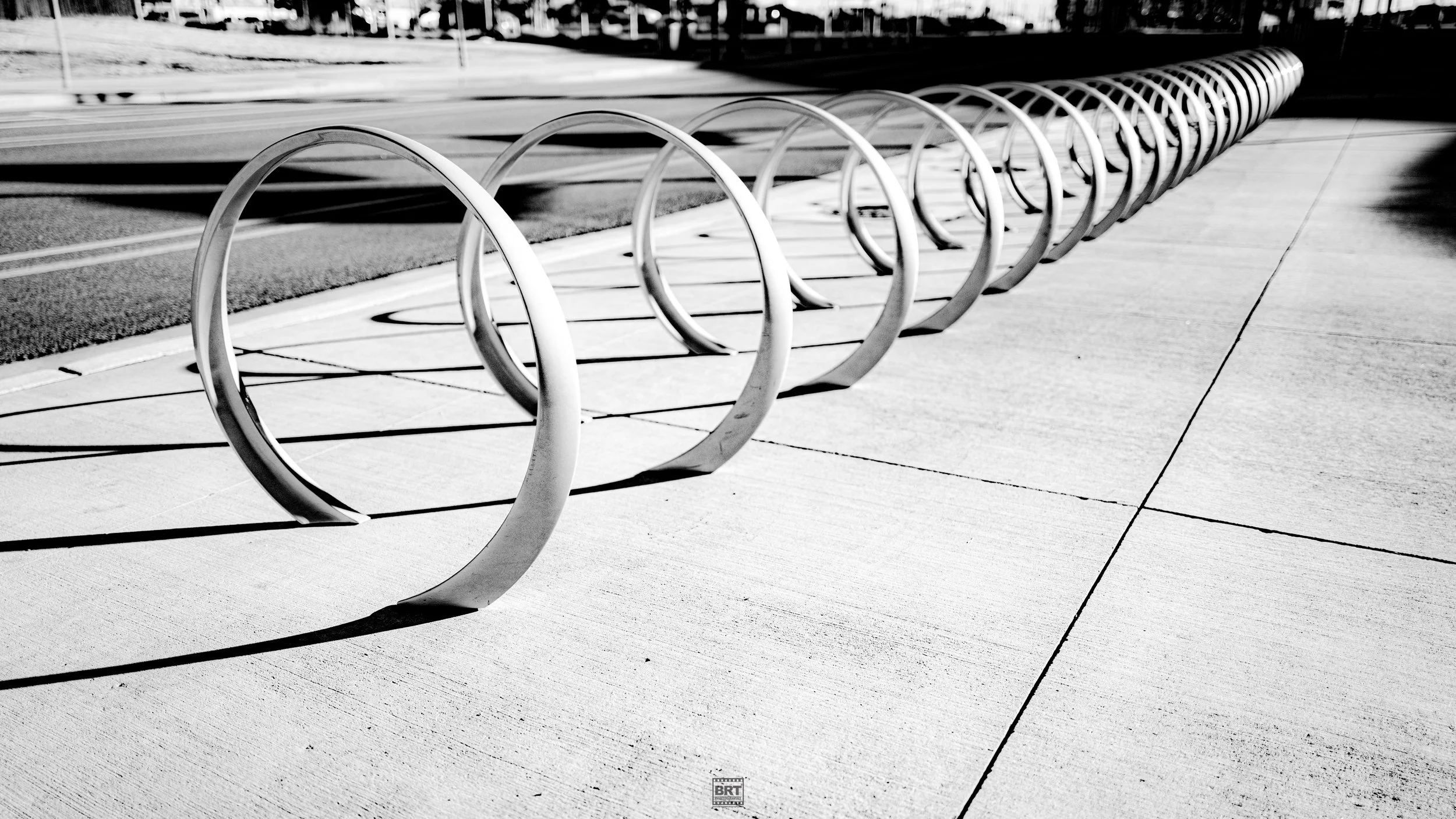 A black and white photo of a row of modern bike racks mounted on a sidewalk next to a street.