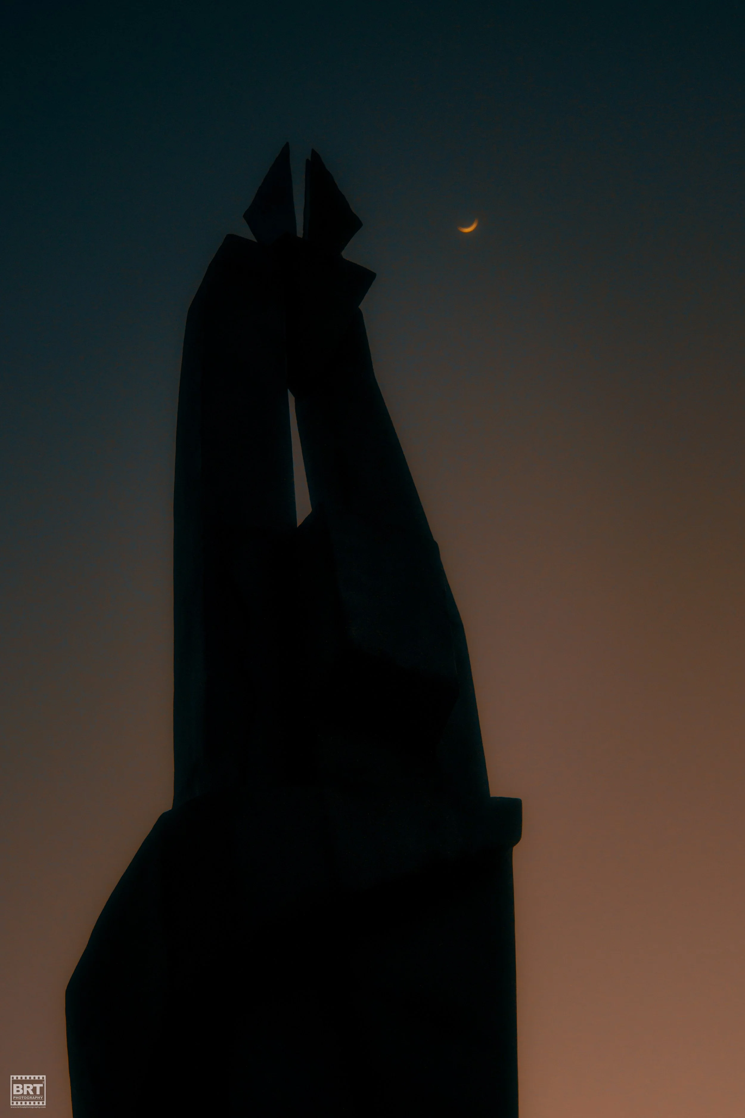 Silhouette of a tall monument against a dusk sky with a crescent moon.