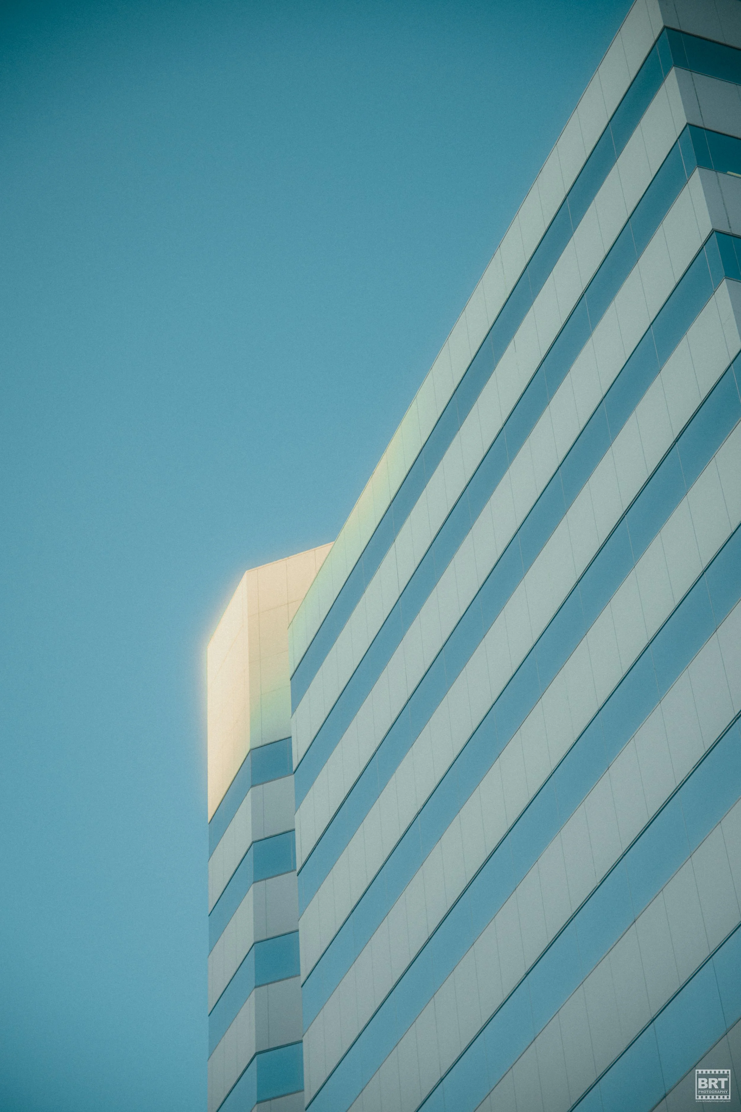 Close-up of a modern glass building with blue-tinted windows and geometric design against a clear blue sky.