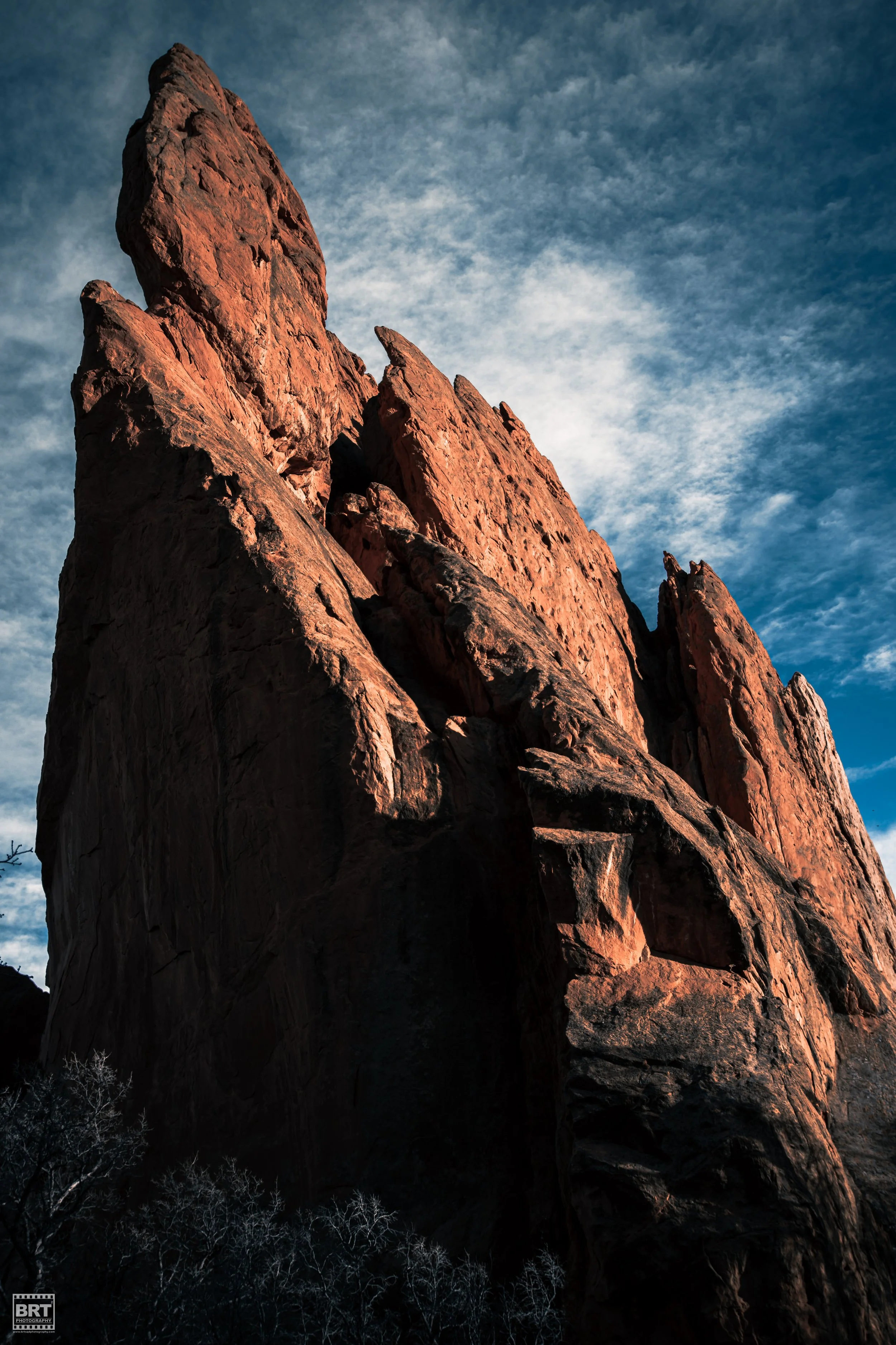A tall, jagged red sandstone cliff against a blue sky with scattered clouds.