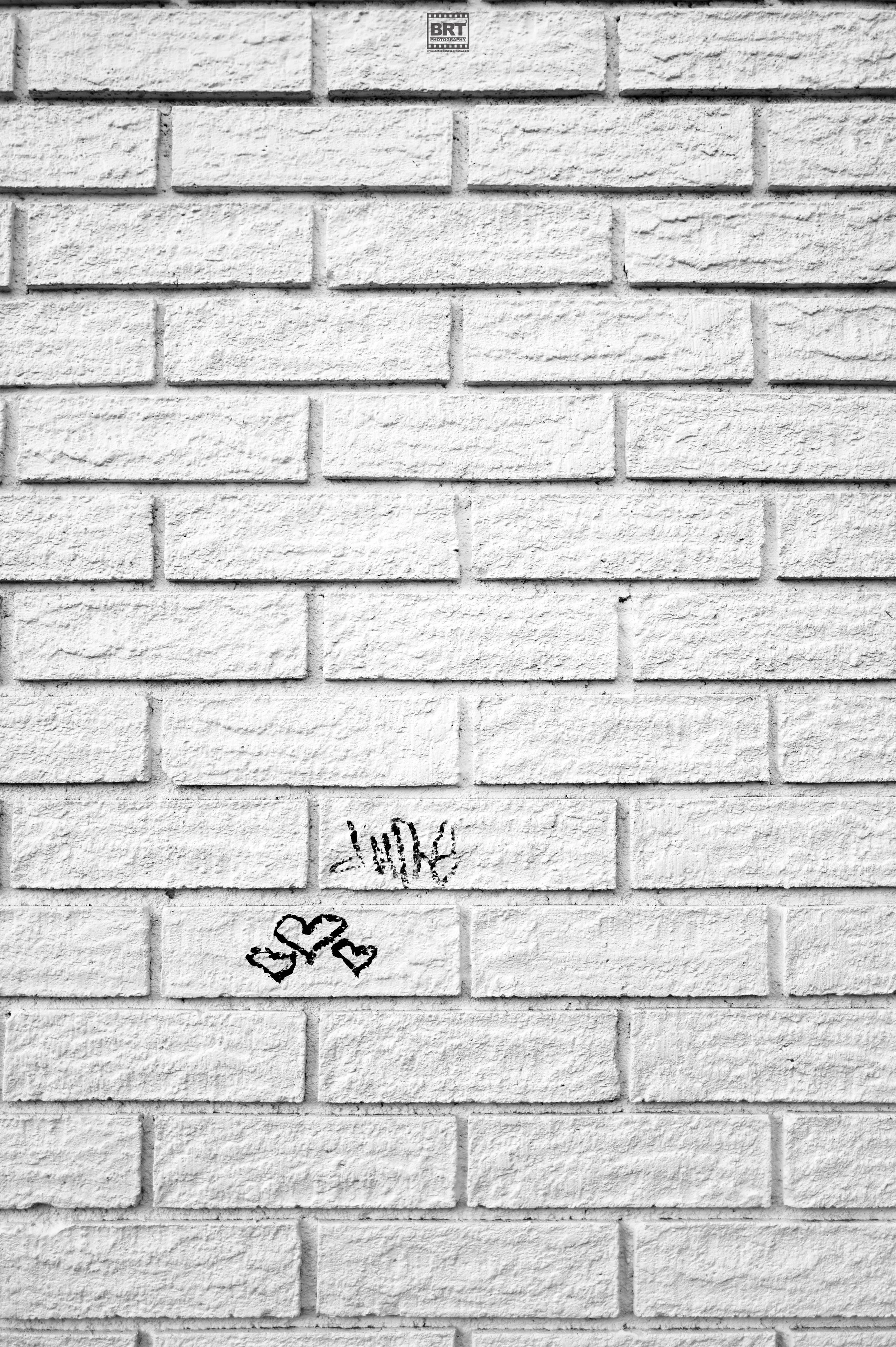 White brick wall with black graffiti writing that says 'Love' and three small hearts.