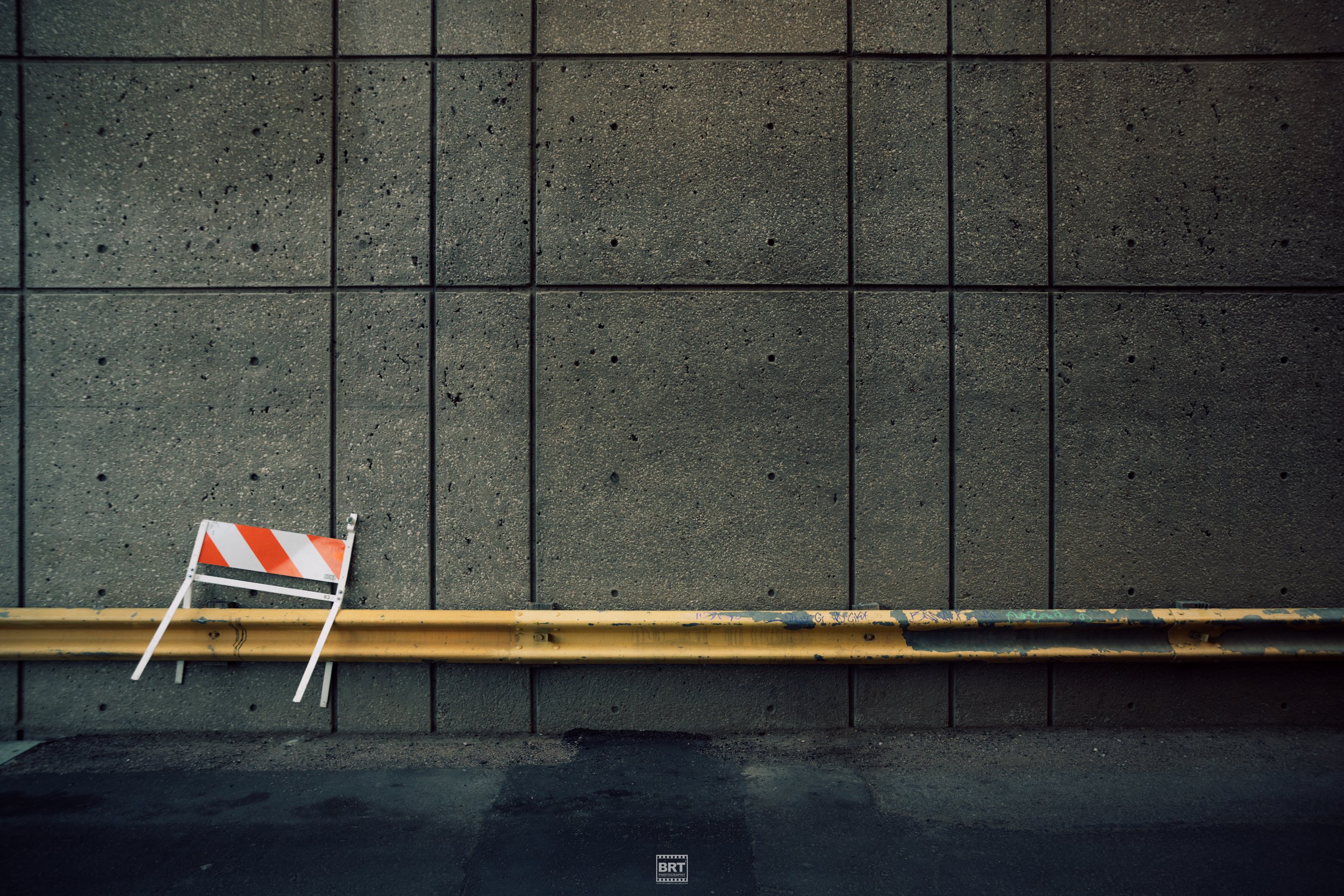 A concrete wall with a horizontal yellow pipe and a small, hinged barricade with orange and white stripes leaning against it.