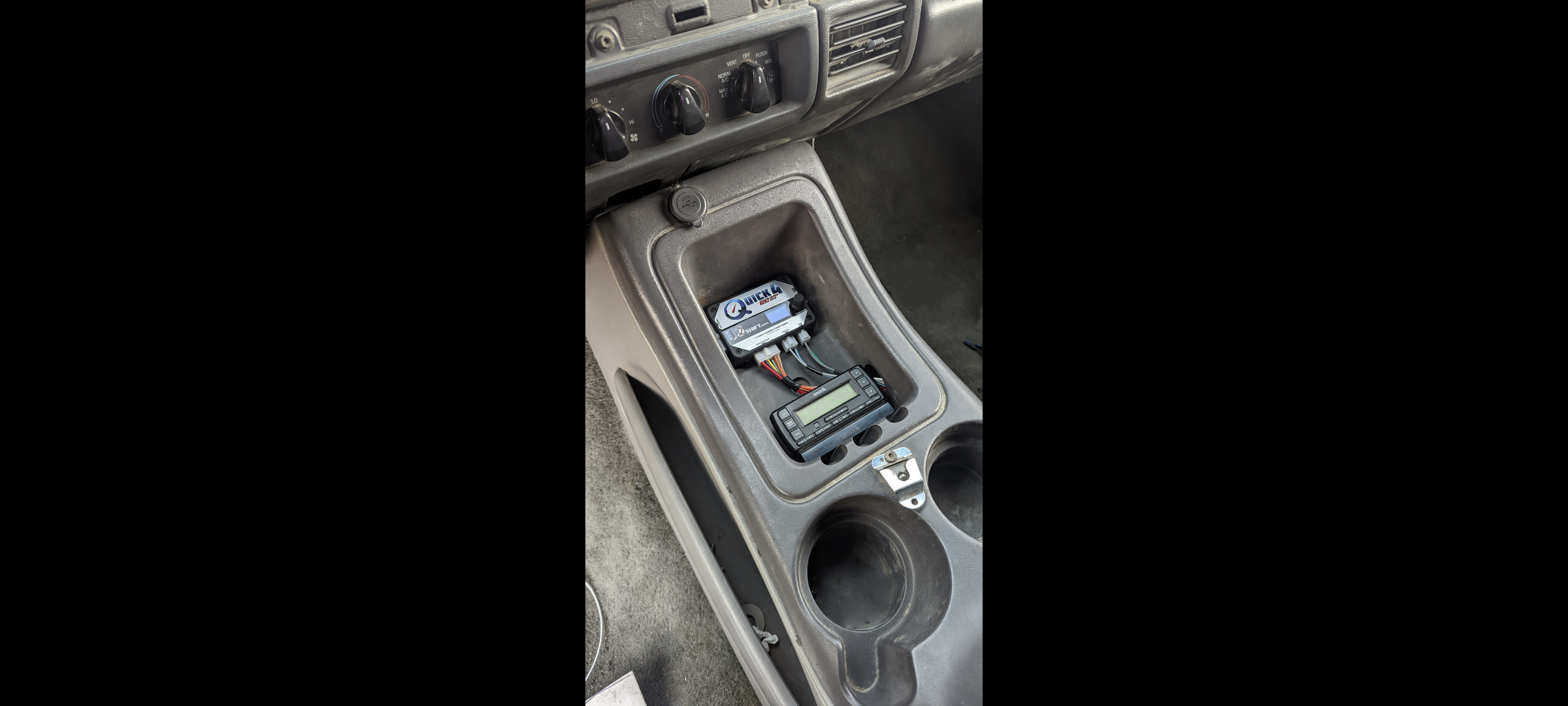 Inside a vehicle's center console, with electronic equipment and wiring placed inside the compartment.