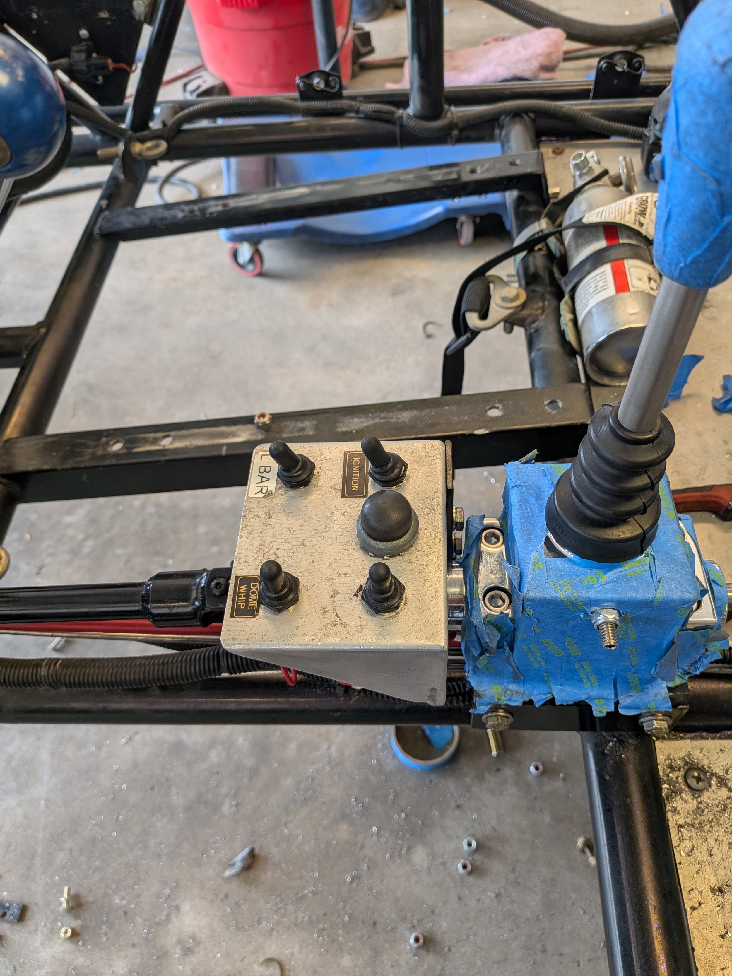 Metal frame of a vehicle with a control box, wires, and mechanical parts, possibly in a workshop or garage.