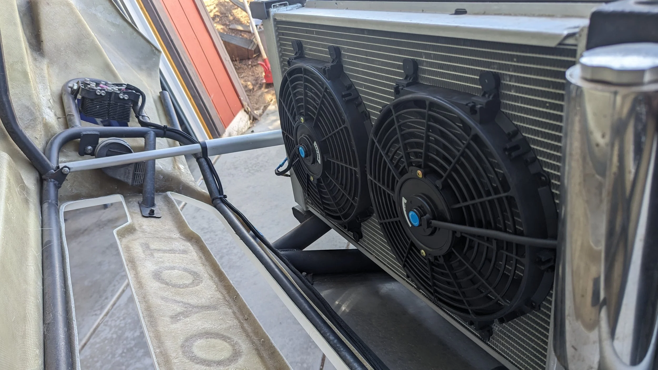 Close-up of a radiator with two attached cooling fans, mounted on a metallic frame with some wires and tools nearby.