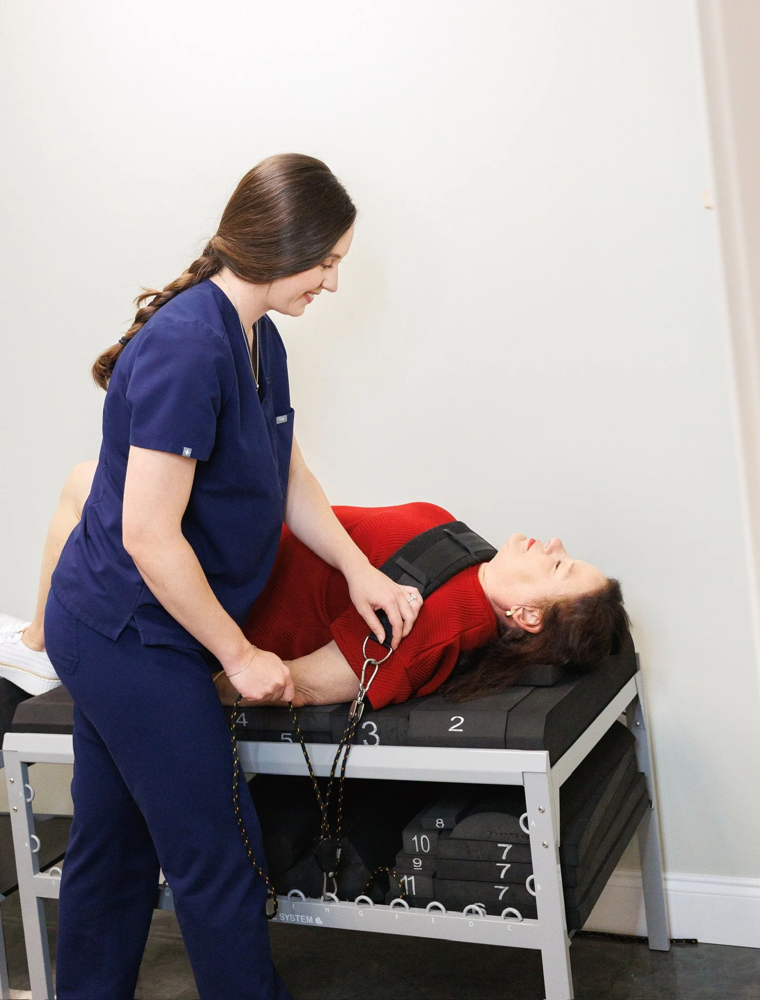 A nurse in blue scrubs checking a patient's blood pressure with a cuff and monitor in a clinical setting.