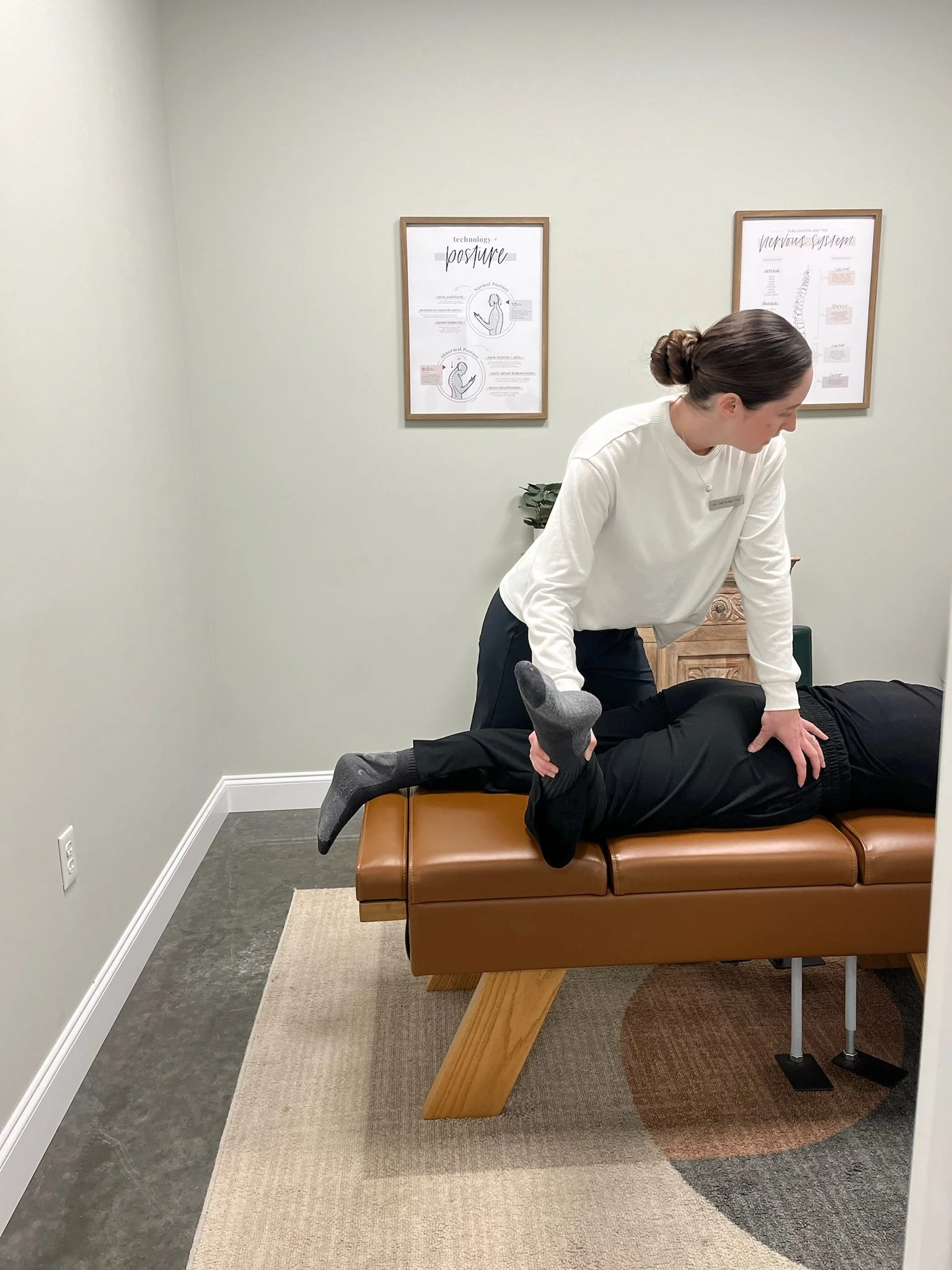A physical therapy or chiropractic session with a therapist performing a lower back adjustment on a patient lying face down on an adjustable treatment table.