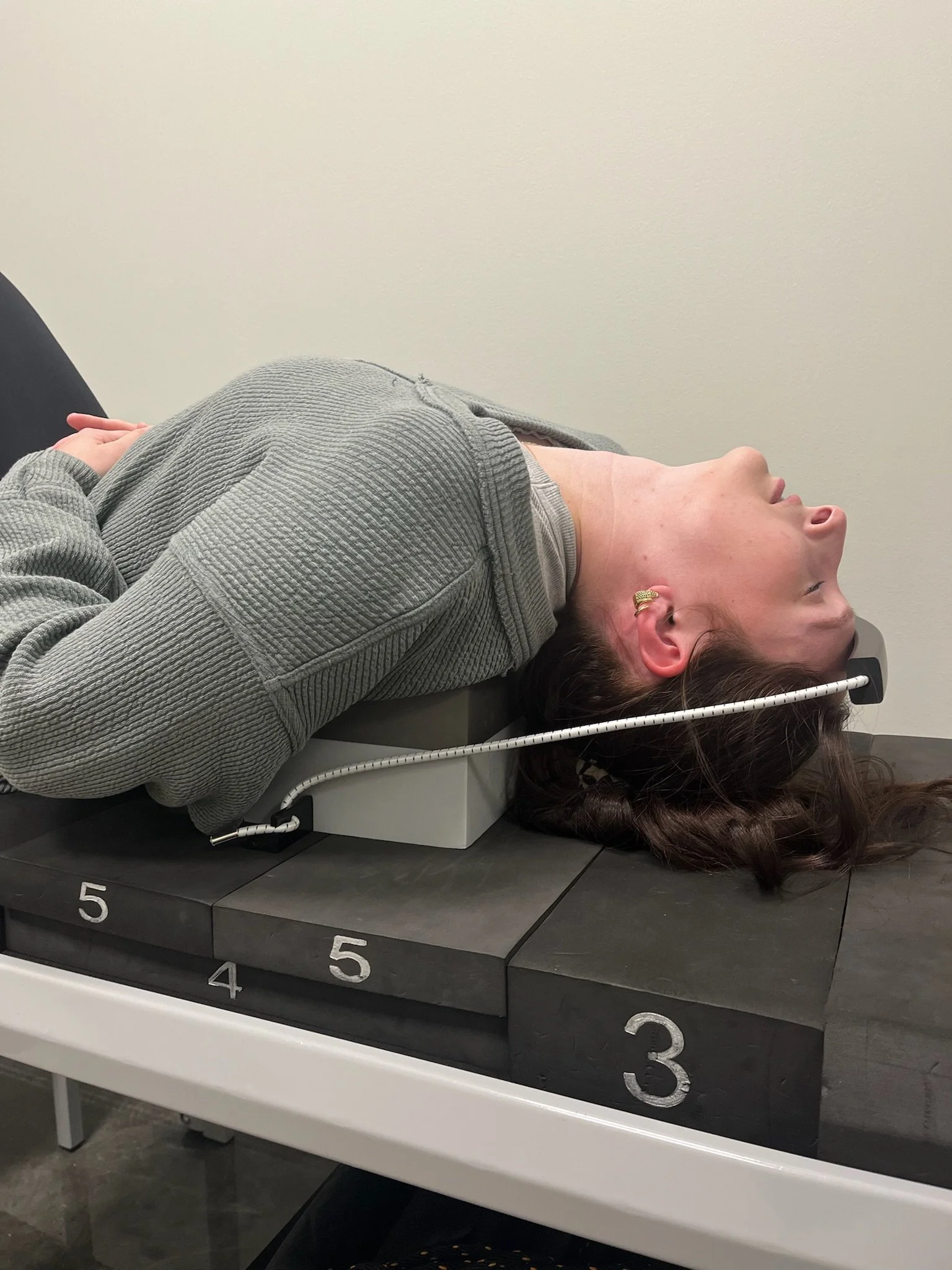 A woman lying on a x-ray table, her head positioned inside an imaging machine, with numbered steps marker on the table.