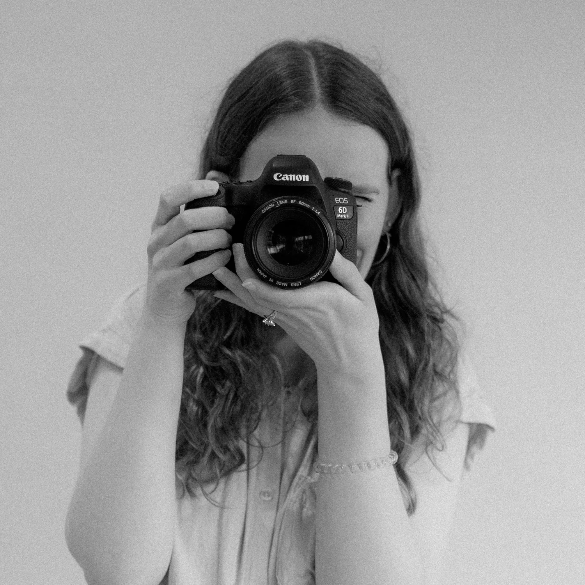 Black and white portrait photo of woman looking through a Canon DSLR camera