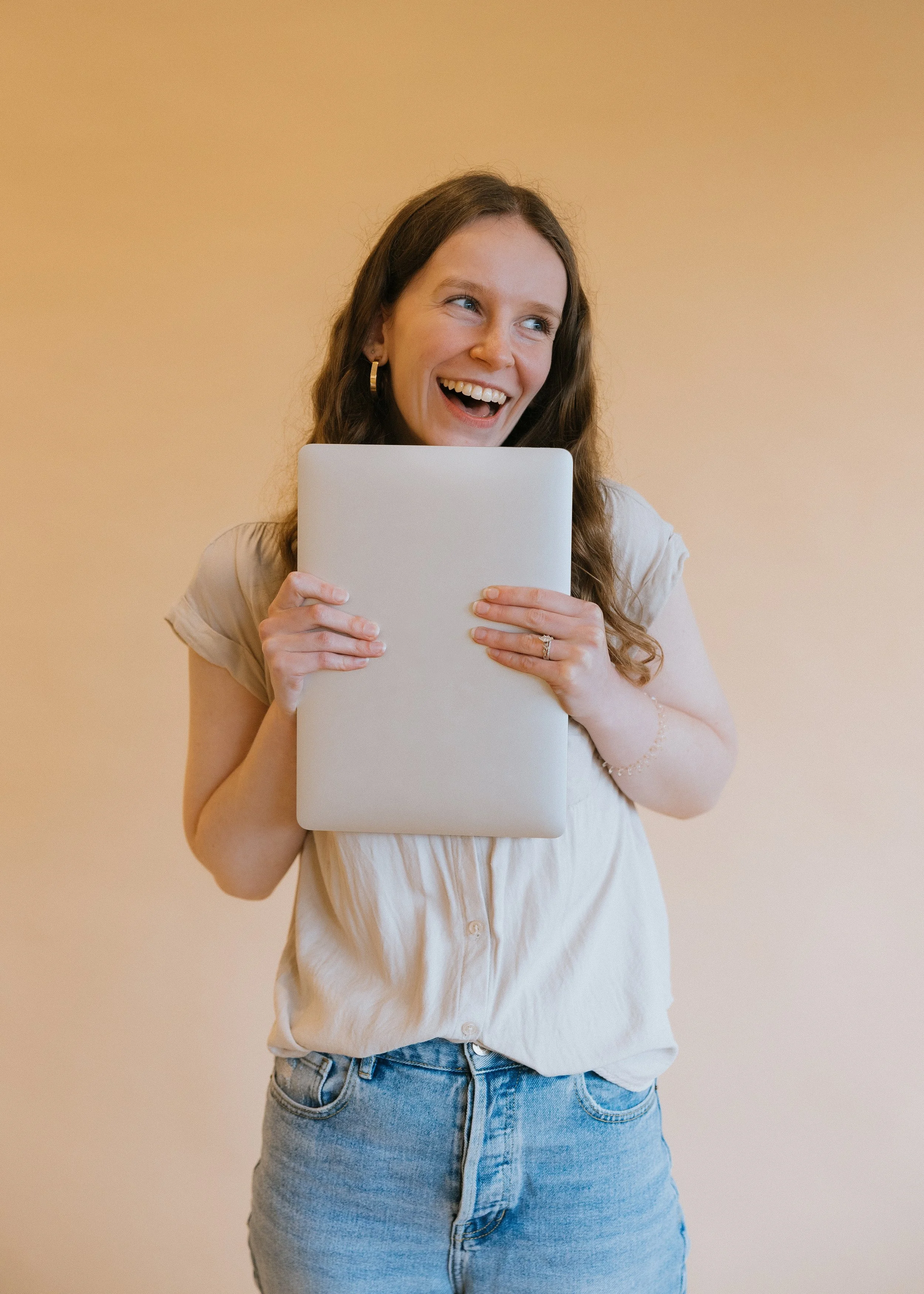 Woman holding laptop just below her chin, looking away from the camerawith a big smile