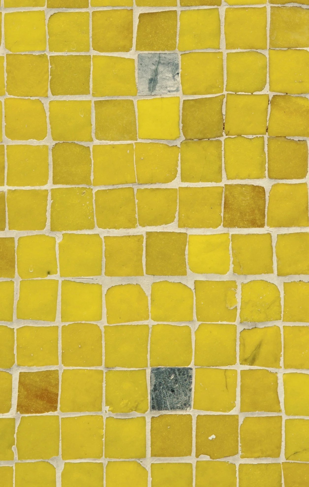 Close-up of a tiled yellow mosaic floor with some gray and darker yellow tiles interspersed among the yellow tiles.