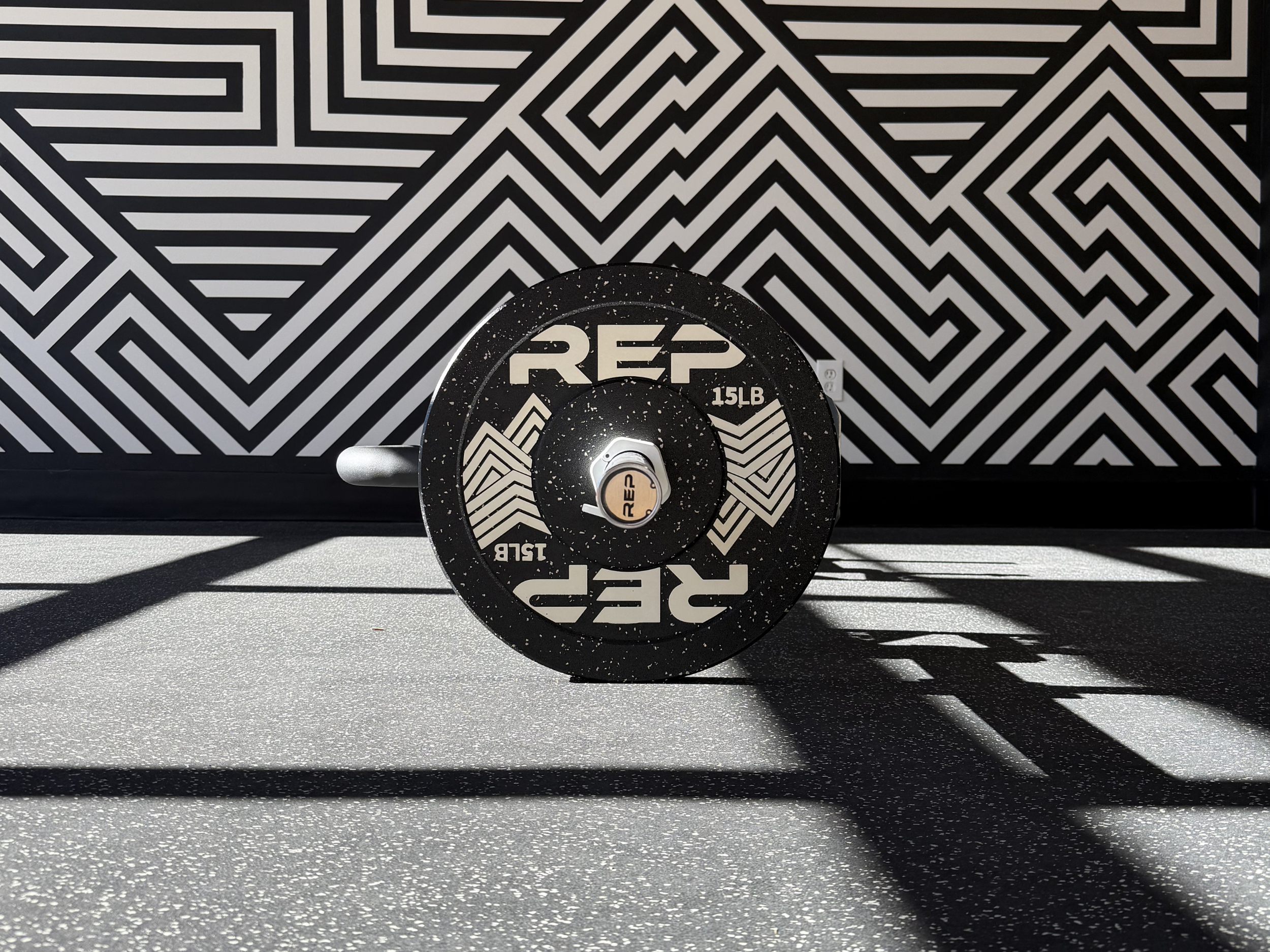 REP barbell with 15 lb weight plate on gym floor inside Proper Fitness personal training studio in Denver’s Santa Fe Arts District.