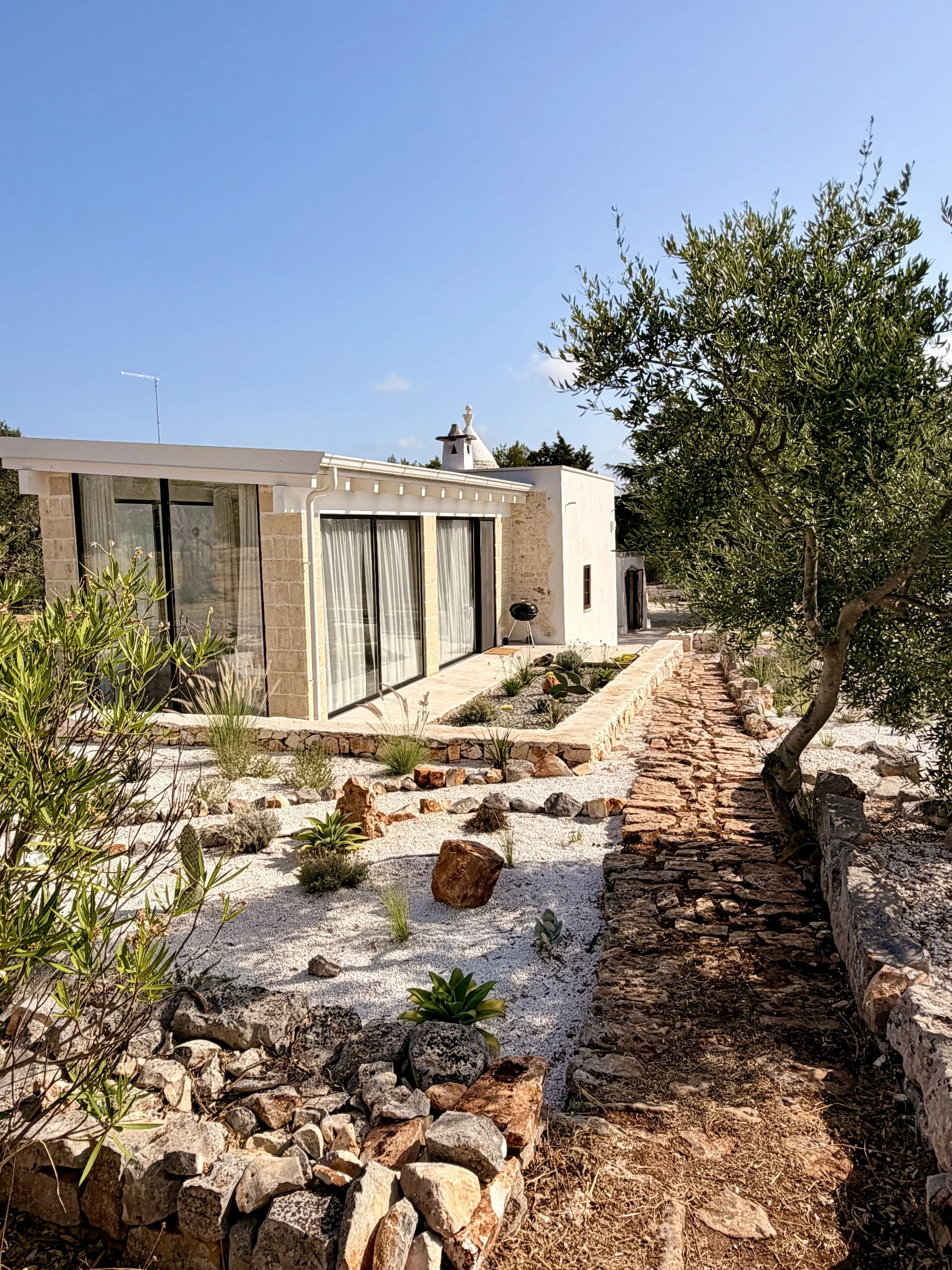 Glass-walled wing and stone garden path at Trullo Ostro