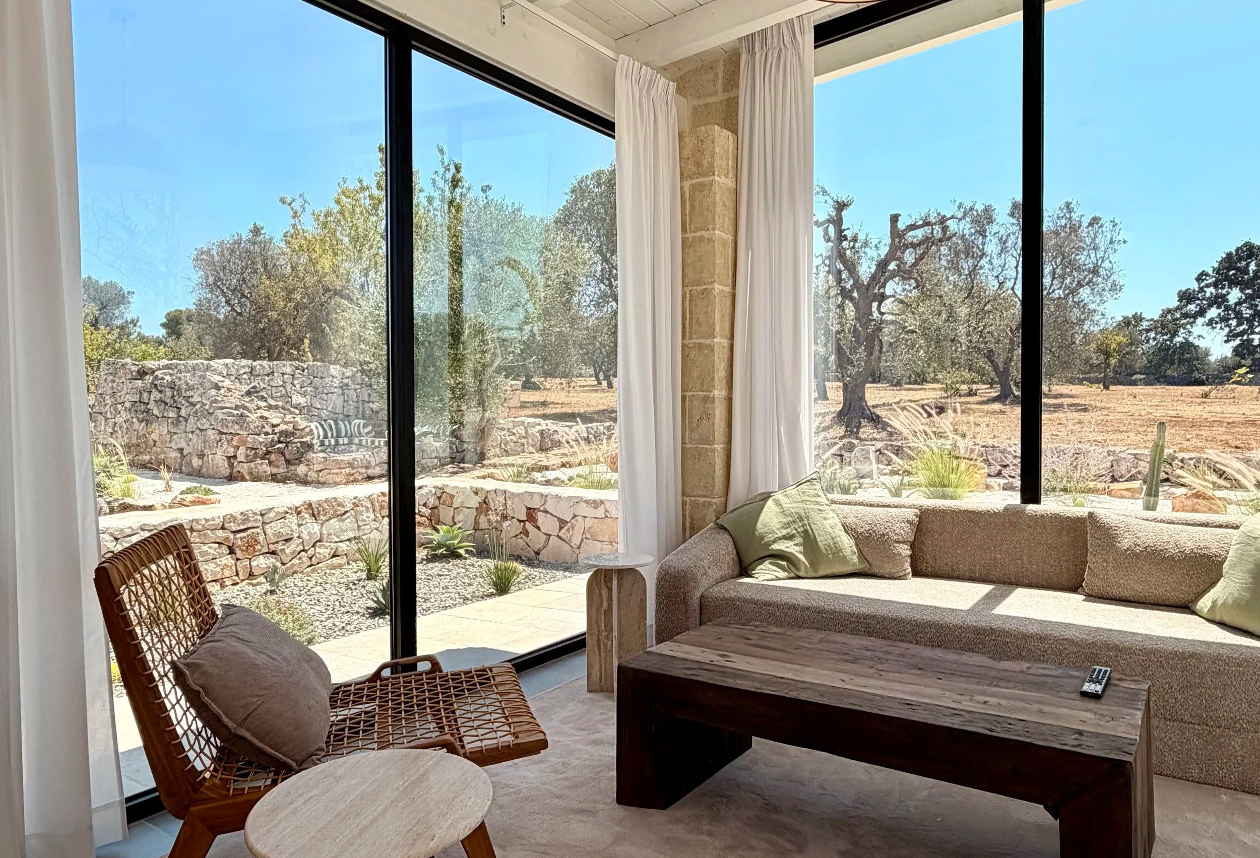 Living room with floor-to-ceiling windows onto the olive garden at Trullo Ostro, Puglia