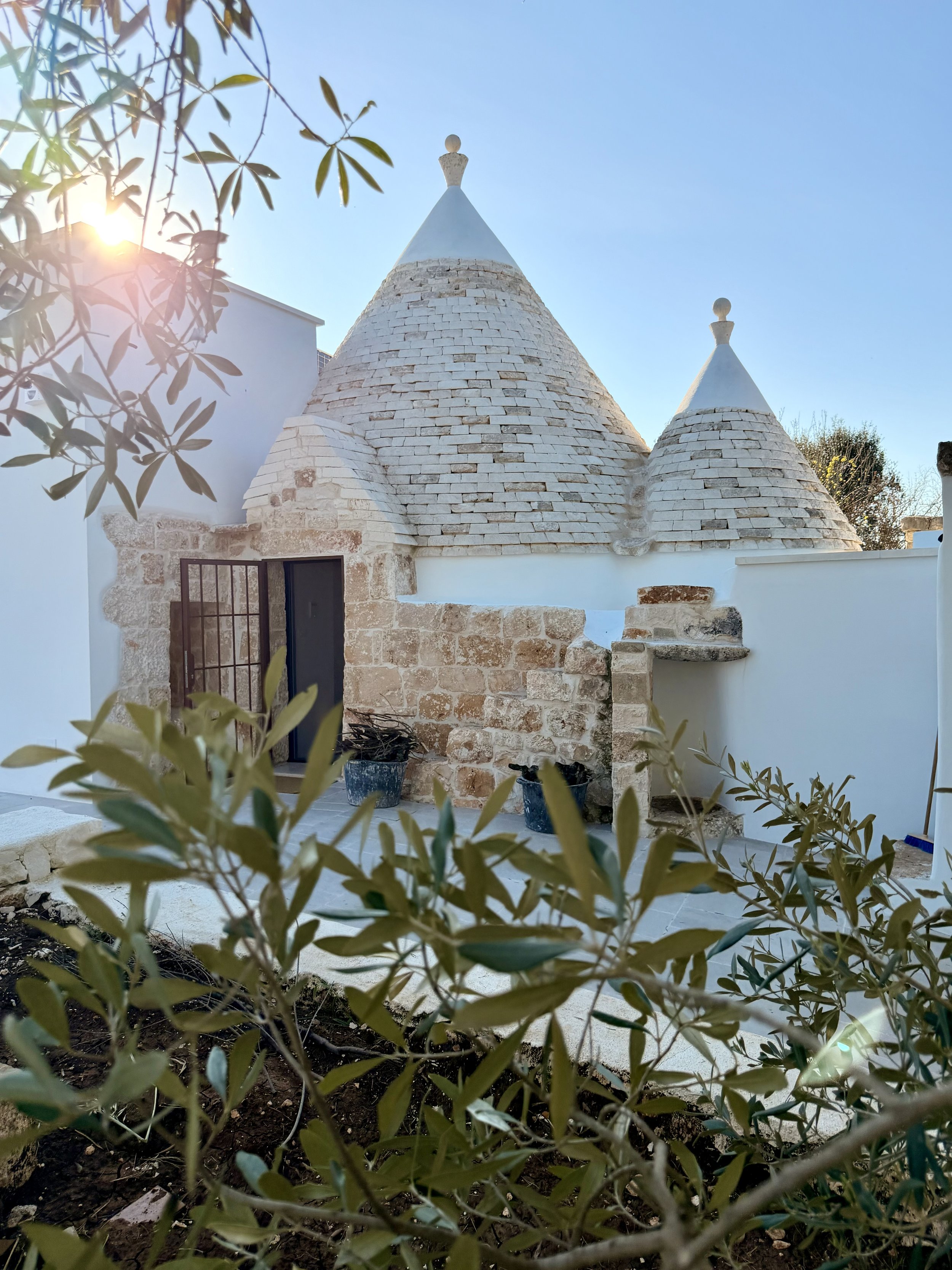Limestone trullo cones framed by olive leaves at Trullo Ostro
