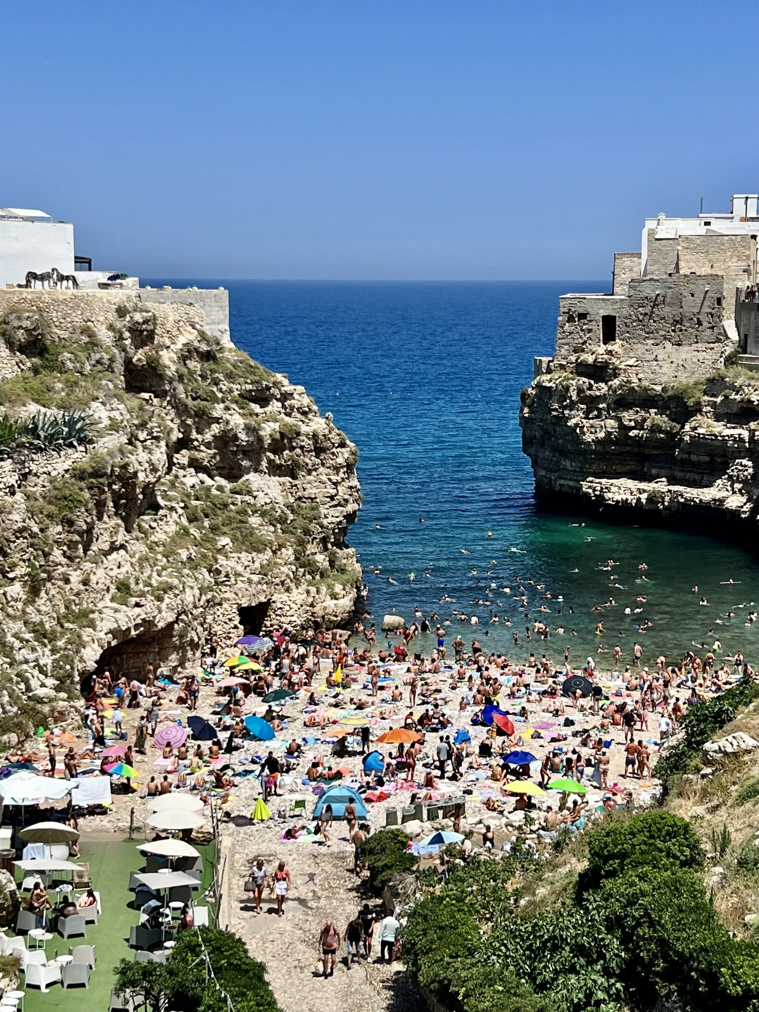 Crowded cove beach between limestone cliffs in Polignano a Mare