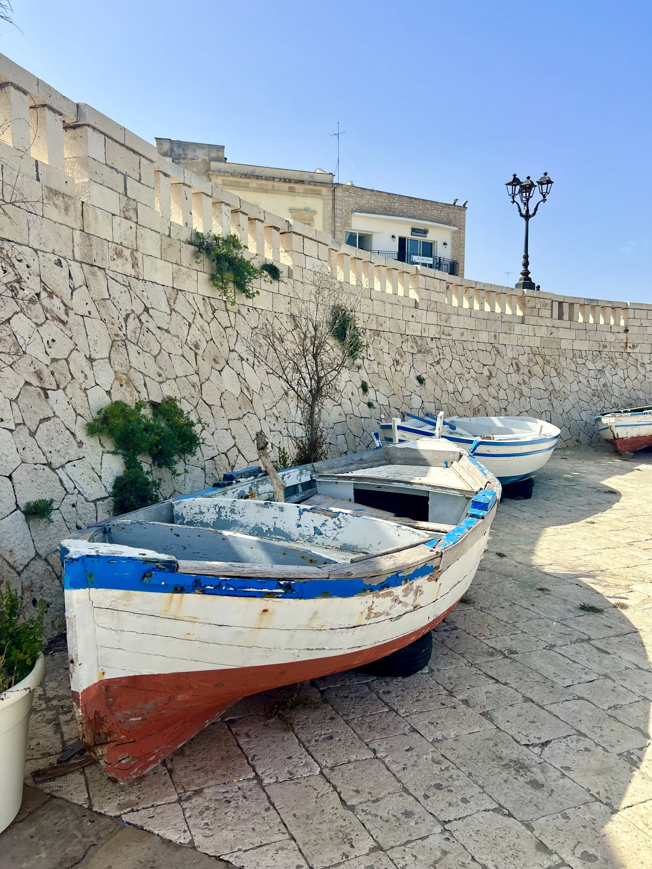 Fishing boats along a stone harbor wall in Puglia