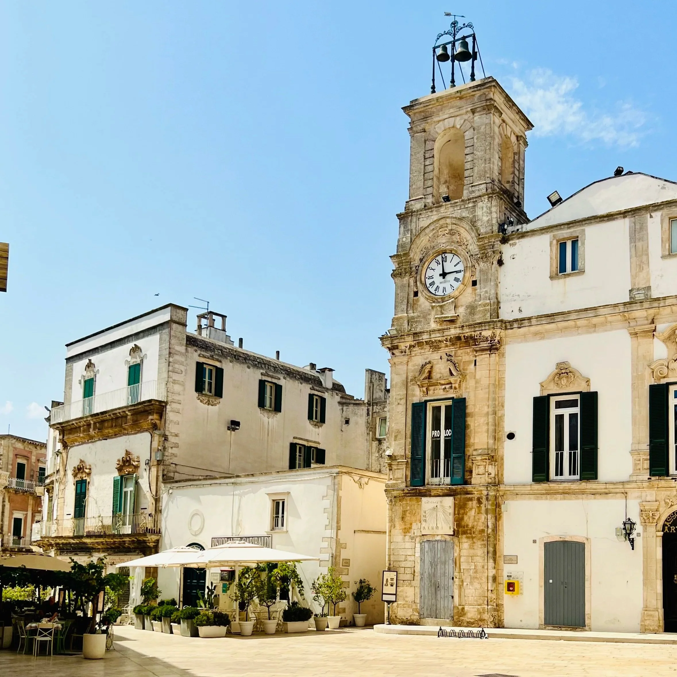 Stone clock tower and whitewashed buildings in a Valle d'Itria town square