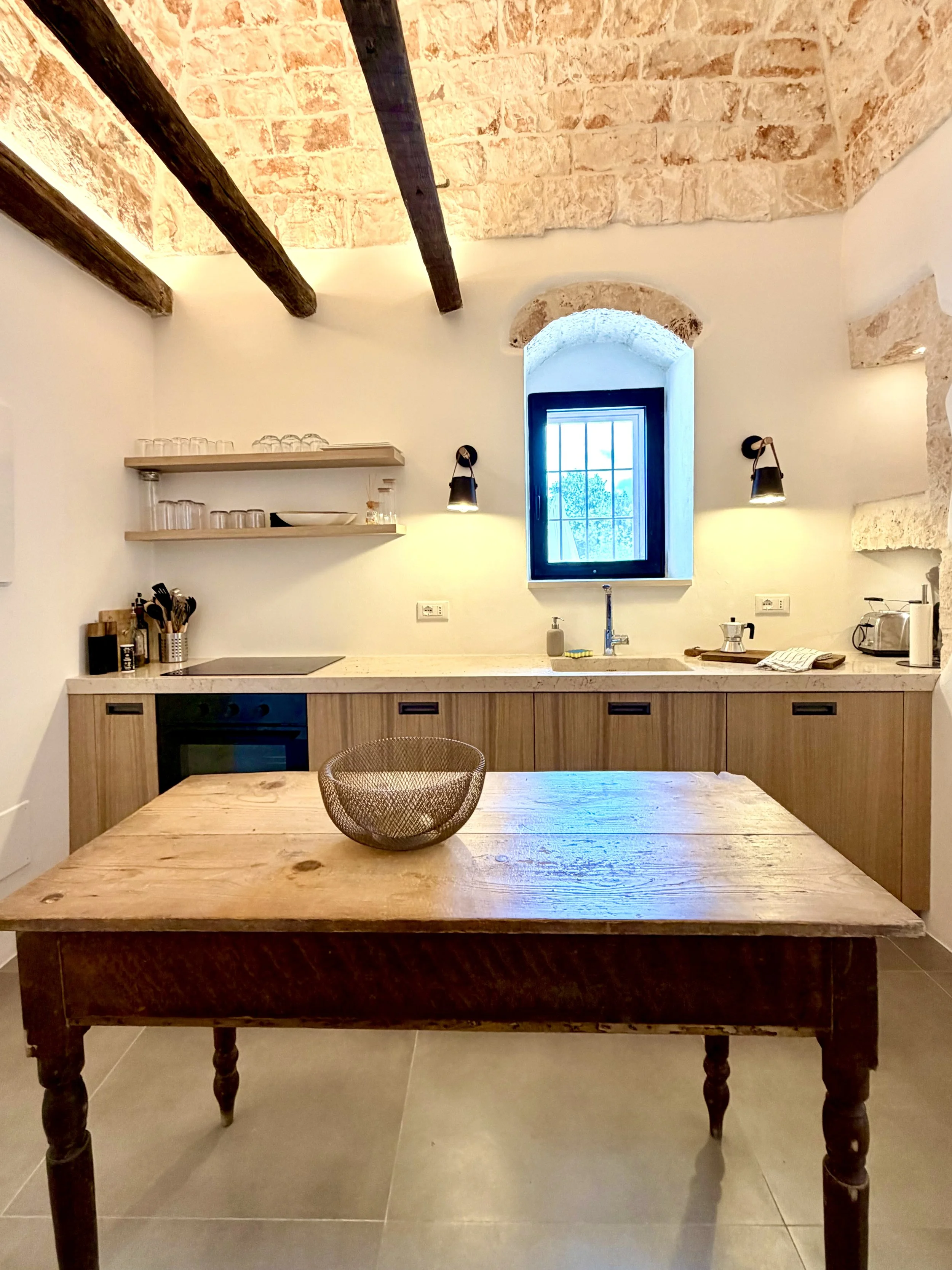Kitchen with wood cabinets and arched window at Trullo Ostro