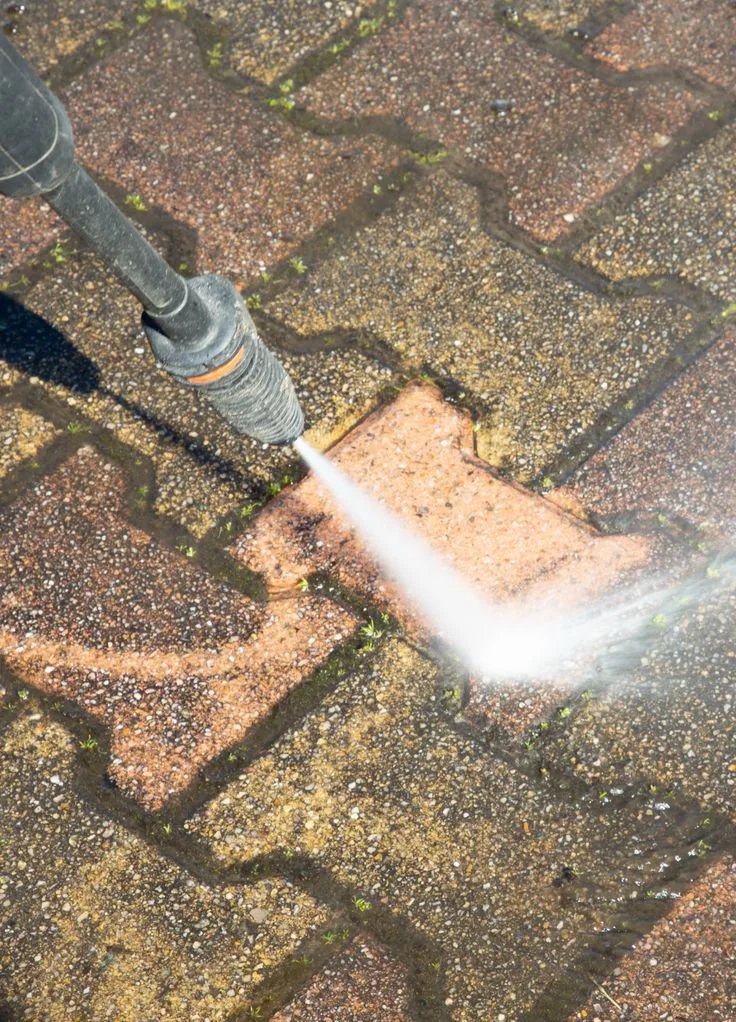 A pressure washer jetting water onto a brick driveway, cleaning the surface.