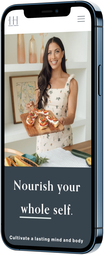 A woman smiling and holding a wooden tray with appetizers or sandwiches, standing in a bright kitchen with decorative vases and artwork in the background.