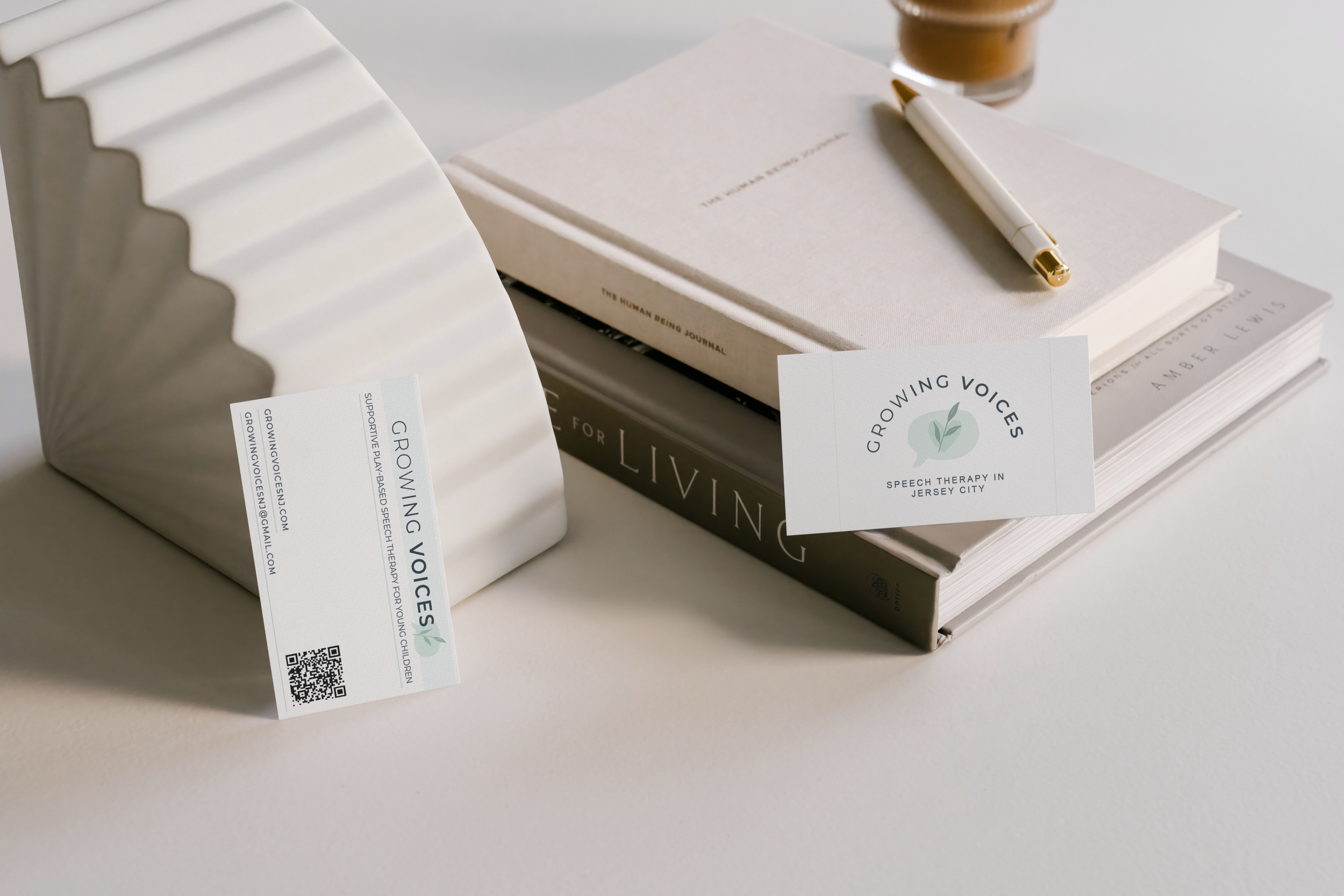 Business card for Growing Voices speech therapy in Jersey City resting on a stack of books with a white pen and a glass of coffee in the background.